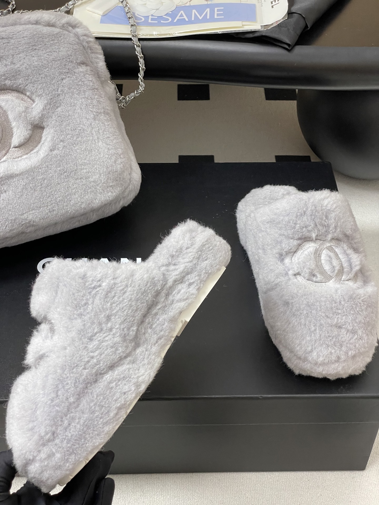 A pair of plush grey faux fur indoor slippers with a white embroidered interlocking circular logo on the top. - Hình 9