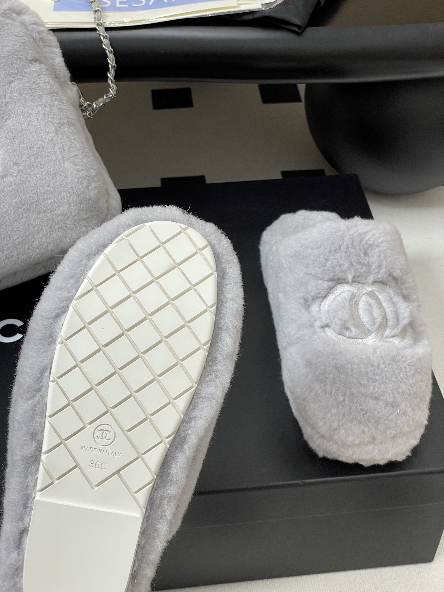 A pair of plush grey faux fur indoor slippers with a white embroidered interlocking circular logo on the top. - Hình 7