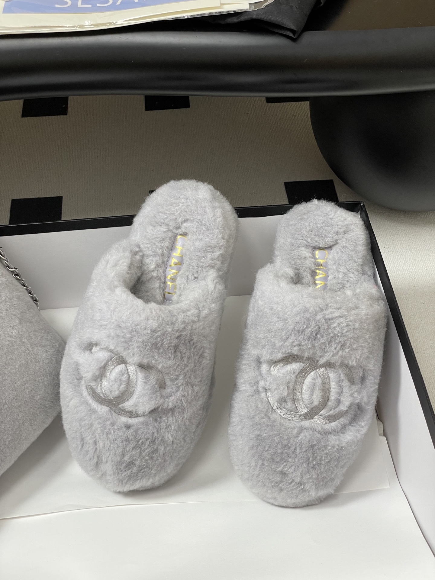 A pair of plush grey faux fur indoor slippers with a white embroidered interlocking circular logo on the top. - Hình 5