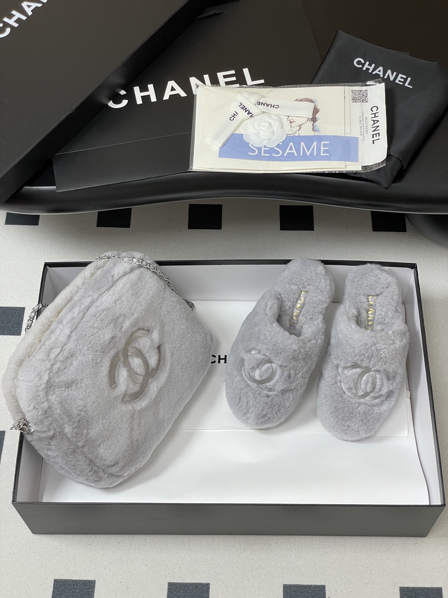 A pair of plush grey faux fur indoor slippers with a white embroidered interlocking circular logo on the top. - Hình 4
