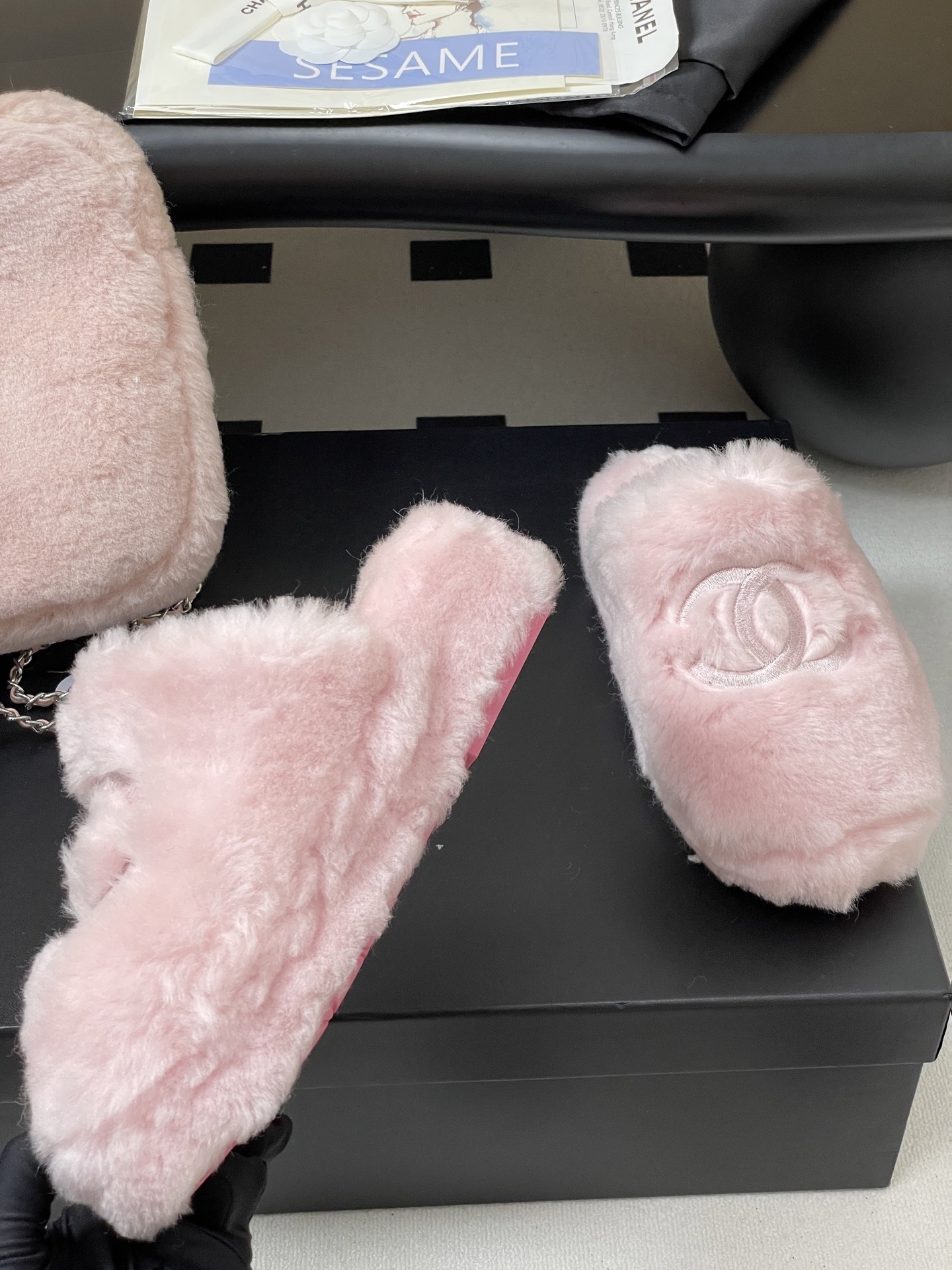 A pair of soft pastel pink Chanel faux fur slippers featuring the embroidered interlocking CC logo on a black surface. - Hình 9