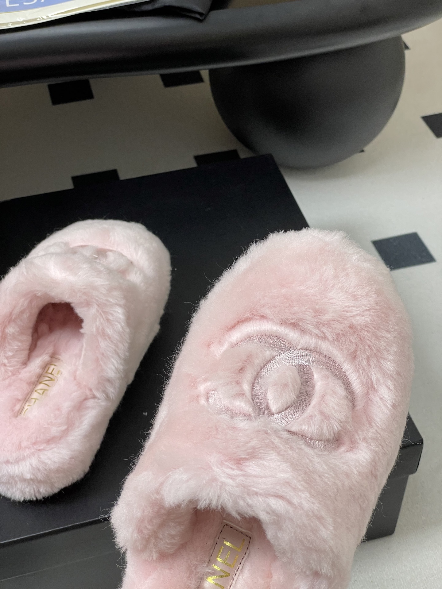 A pair of soft pastel pink Chanel faux fur slippers featuring the embroidered interlocking CC logo on a black surface. - Hình 8