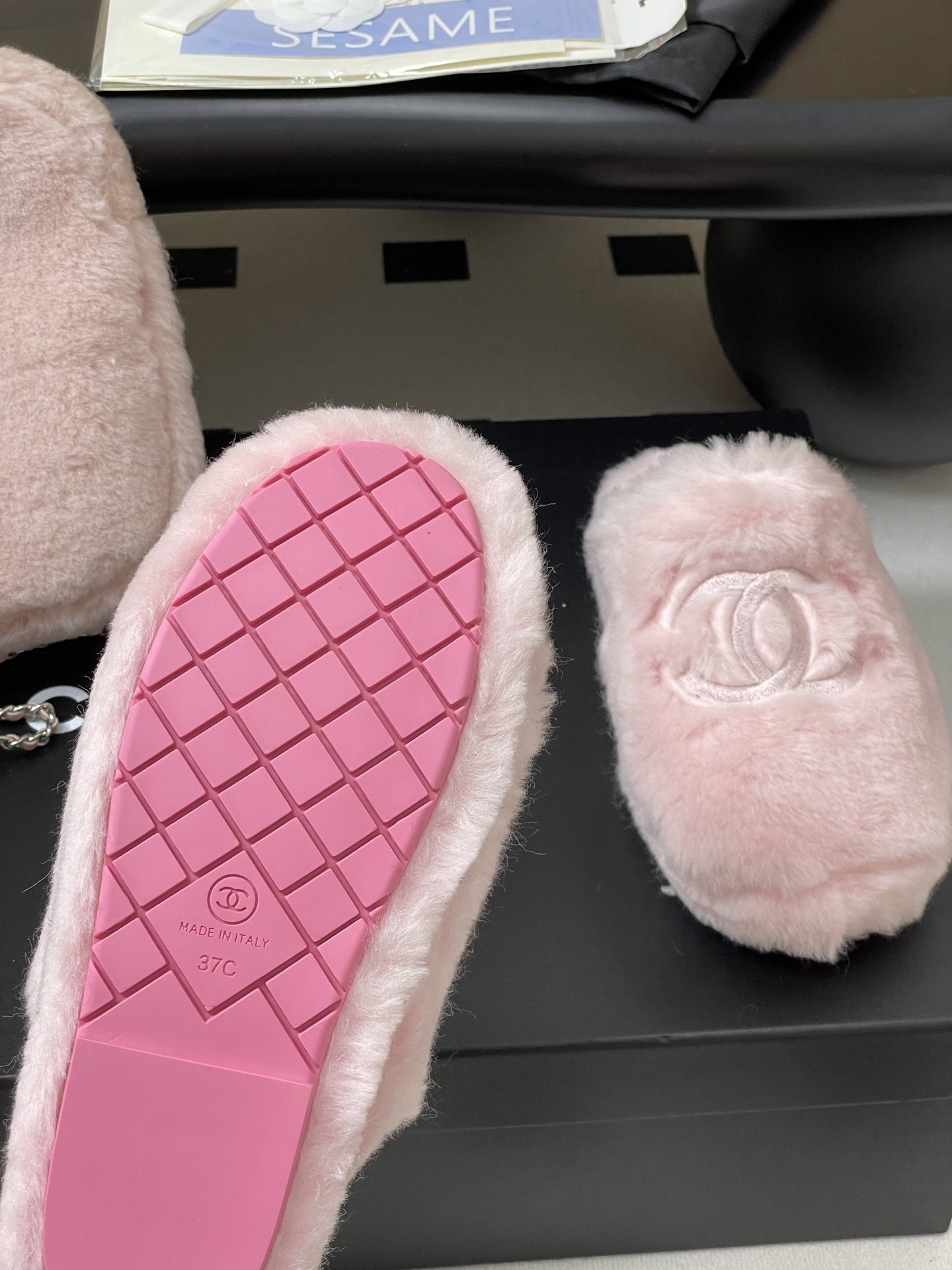 A pair of soft pastel pink Chanel faux fur slippers featuring the embroidered interlocking CC logo on a black surface. - Hình 7