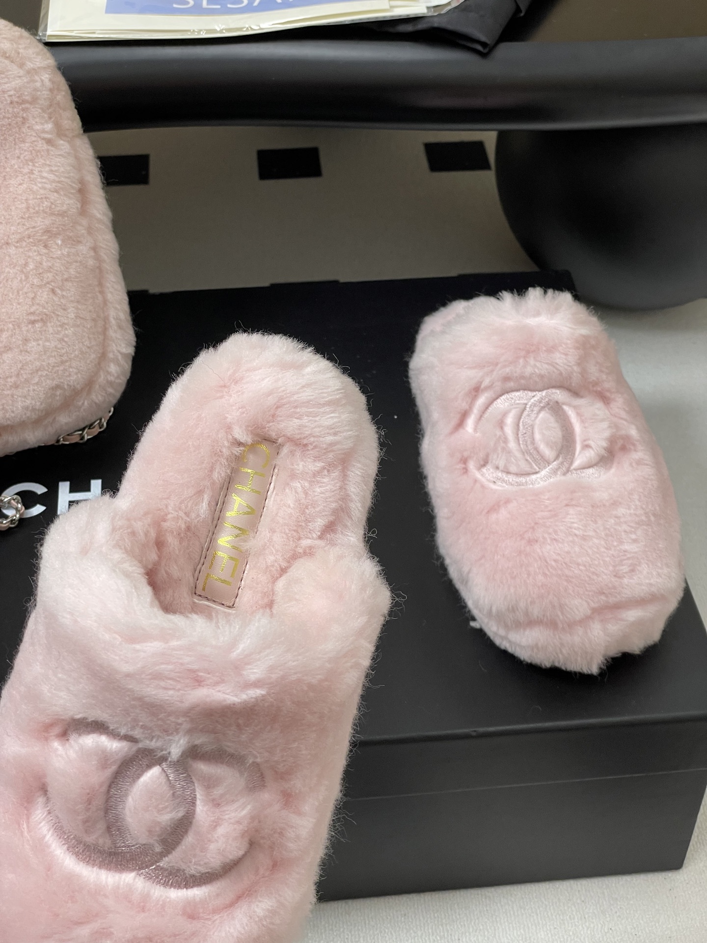 A pair of soft pastel pink Chanel faux fur slippers featuring the embroidered interlocking CC logo on a black surface. - Hình 6