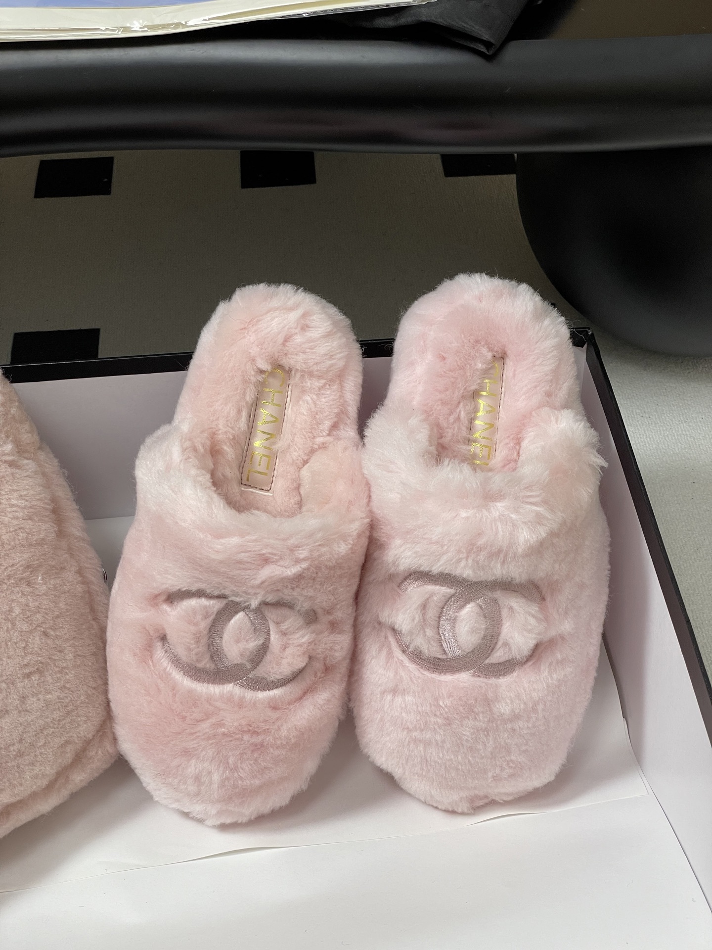 A pair of soft pastel pink Chanel faux fur slippers featuring the embroidered interlocking CC logo on a black surface. - Hình 5