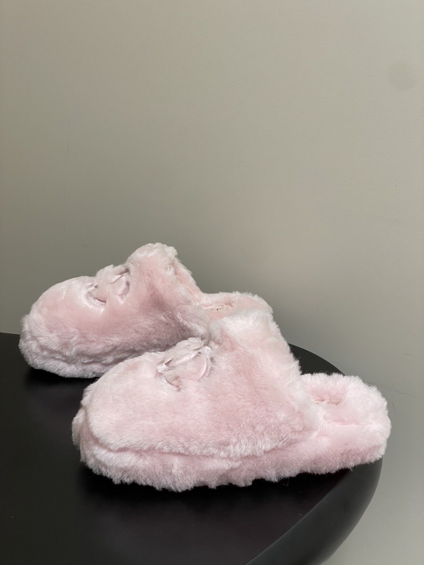 A pair of soft pastel pink Chanel faux fur slippers featuring the embroidered interlocking CC logo on a black surface. - Hình 3