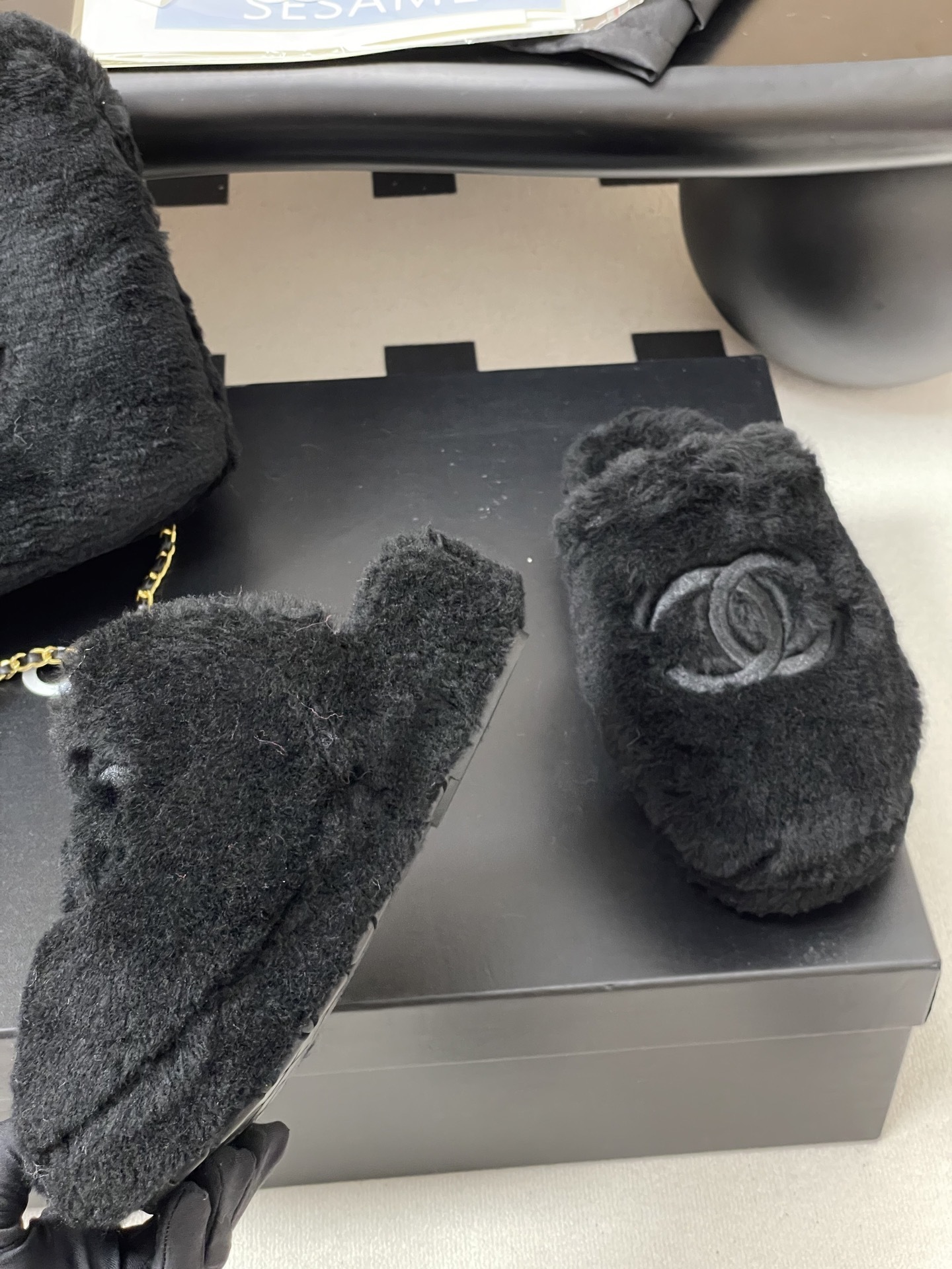 Pair of black plush fuzzy slippers with a grey interlocking CC logo on a black surface - Hình 9