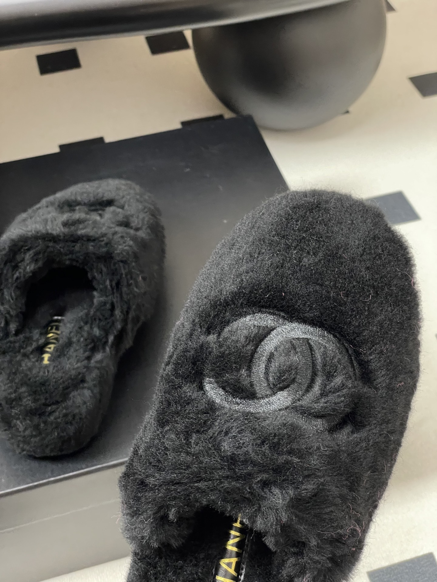 Pair of black plush fuzzy slippers with a grey interlocking CC logo on a black surface - Hình 8