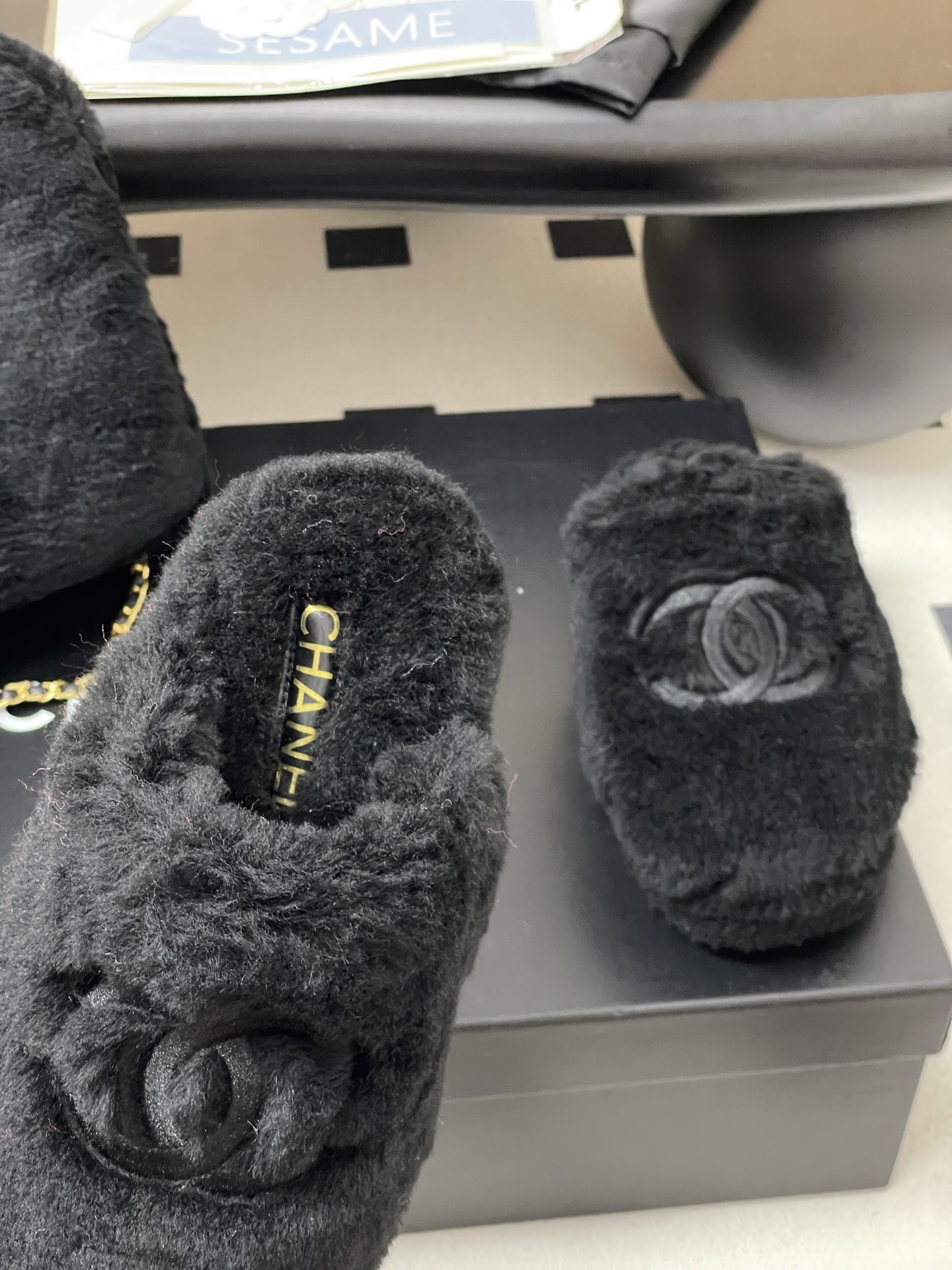 Pair of black plush fuzzy slippers with a grey interlocking CC logo on a black surface - Hình 6