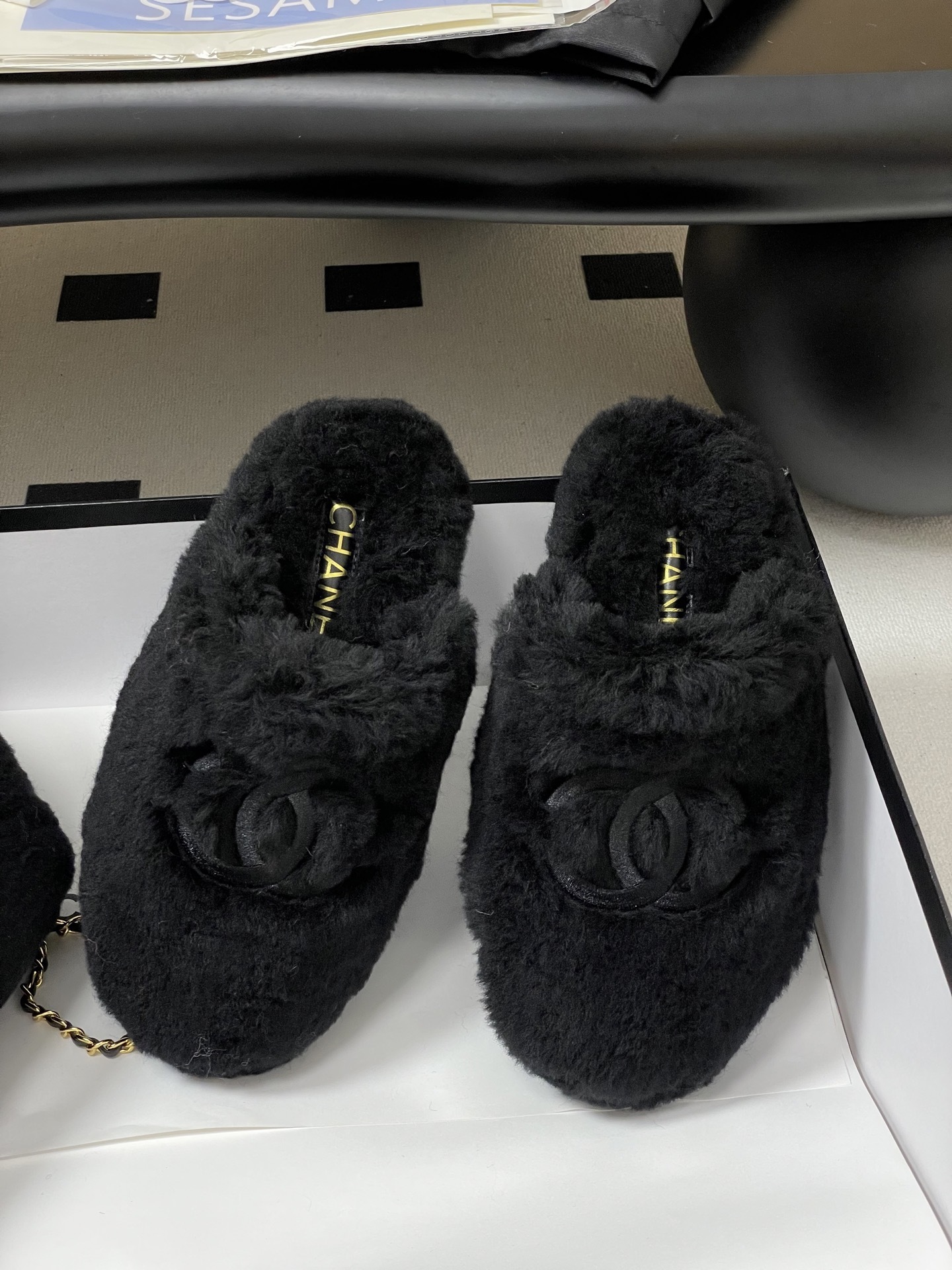 Pair of black plush fuzzy slippers with a grey interlocking CC logo on a black surface - Hình 5