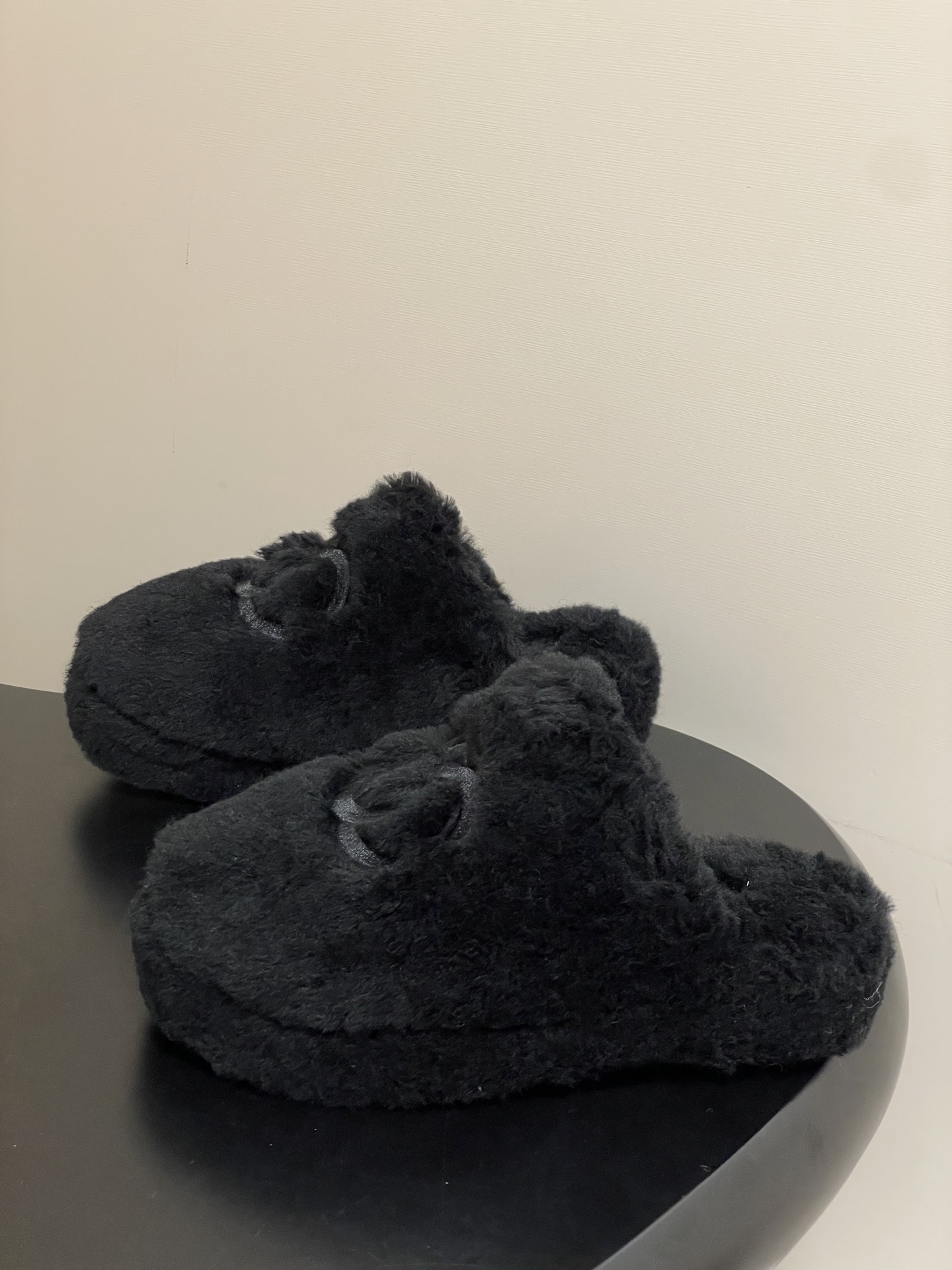 Pair of black plush fuzzy slippers with a grey interlocking CC logo on a black surface - Hình 3