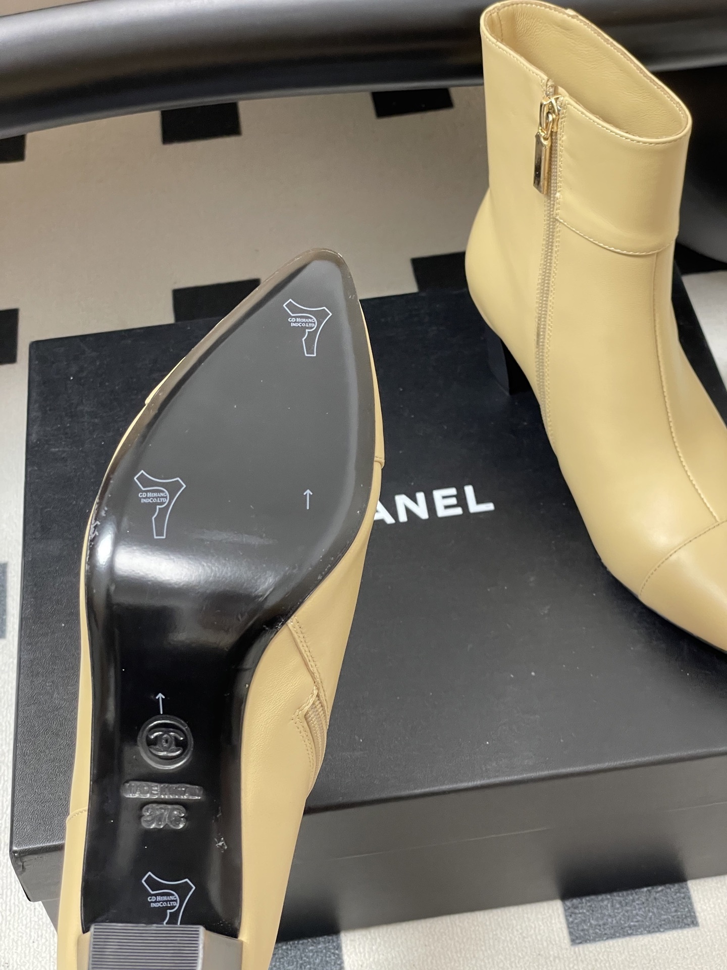 Pair of elegant beige leather ankle boots with a gold lion head embellishment and pointed toe on a black surface. - Hình 7