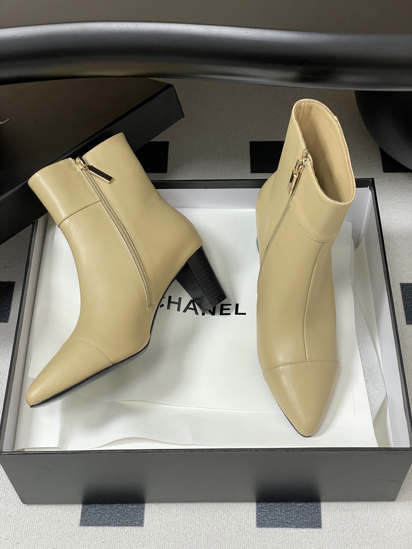 Pair of elegant beige leather ankle boots with a gold lion head embellishment and pointed toe on a black surface. - Hình 6