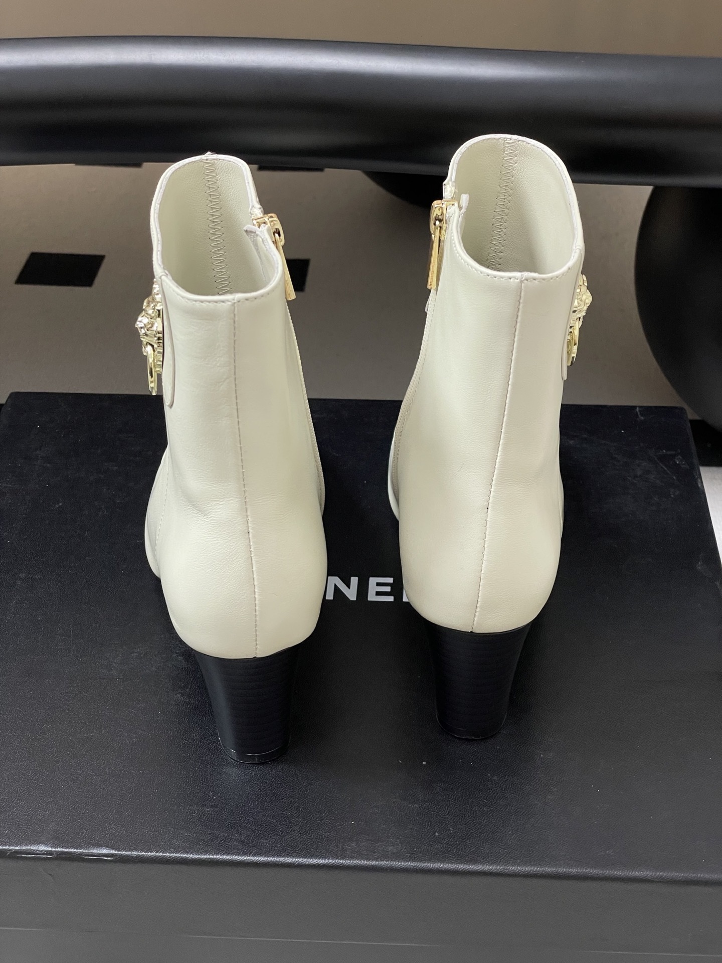 Pair of creamy white leather ankle boots with gold lion head hardware and pointed toe on a black surface - Hình 9