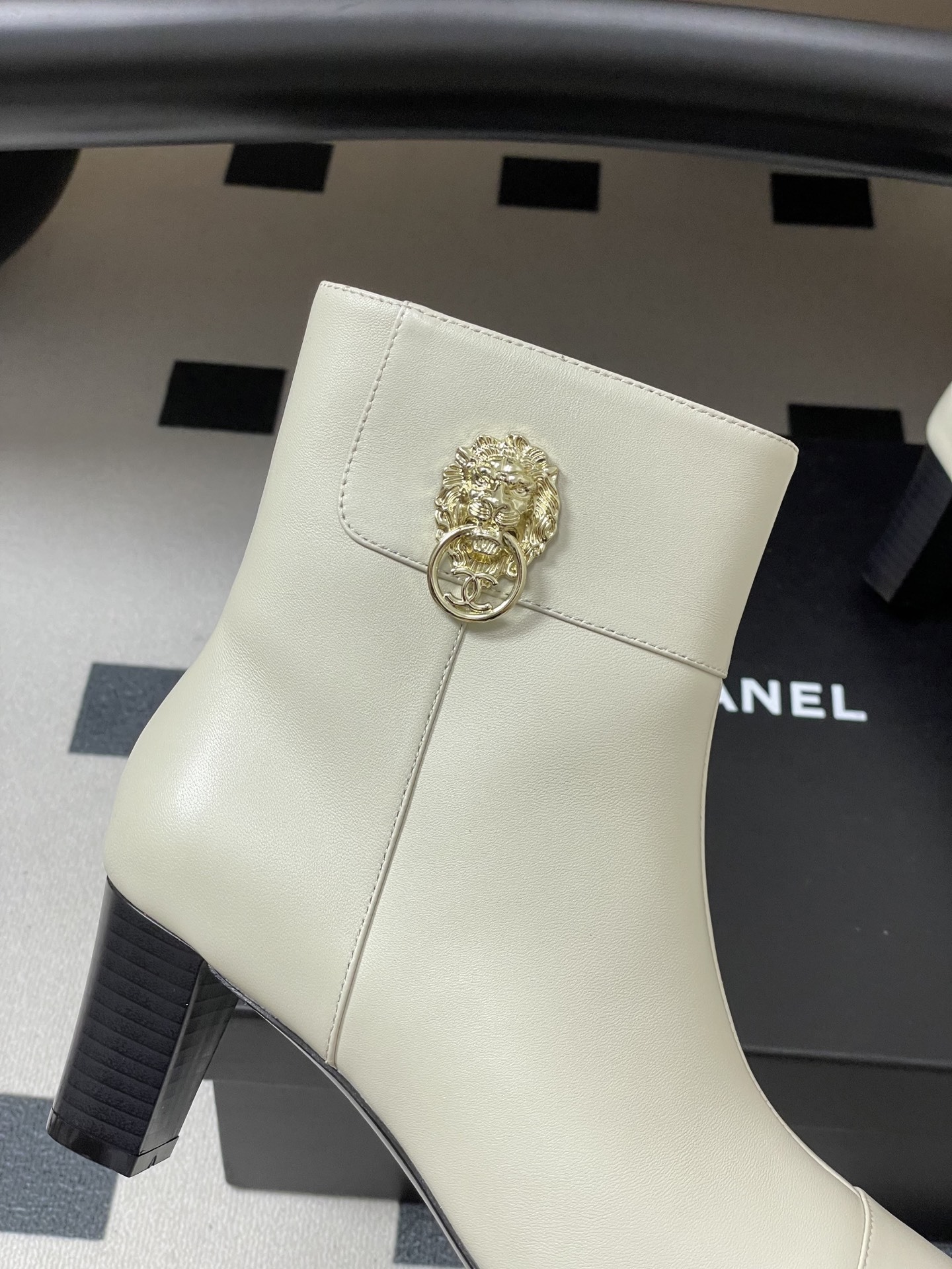 Pair of creamy white leather ankle boots with gold lion head hardware and pointed toe on a black surface - Hình 8