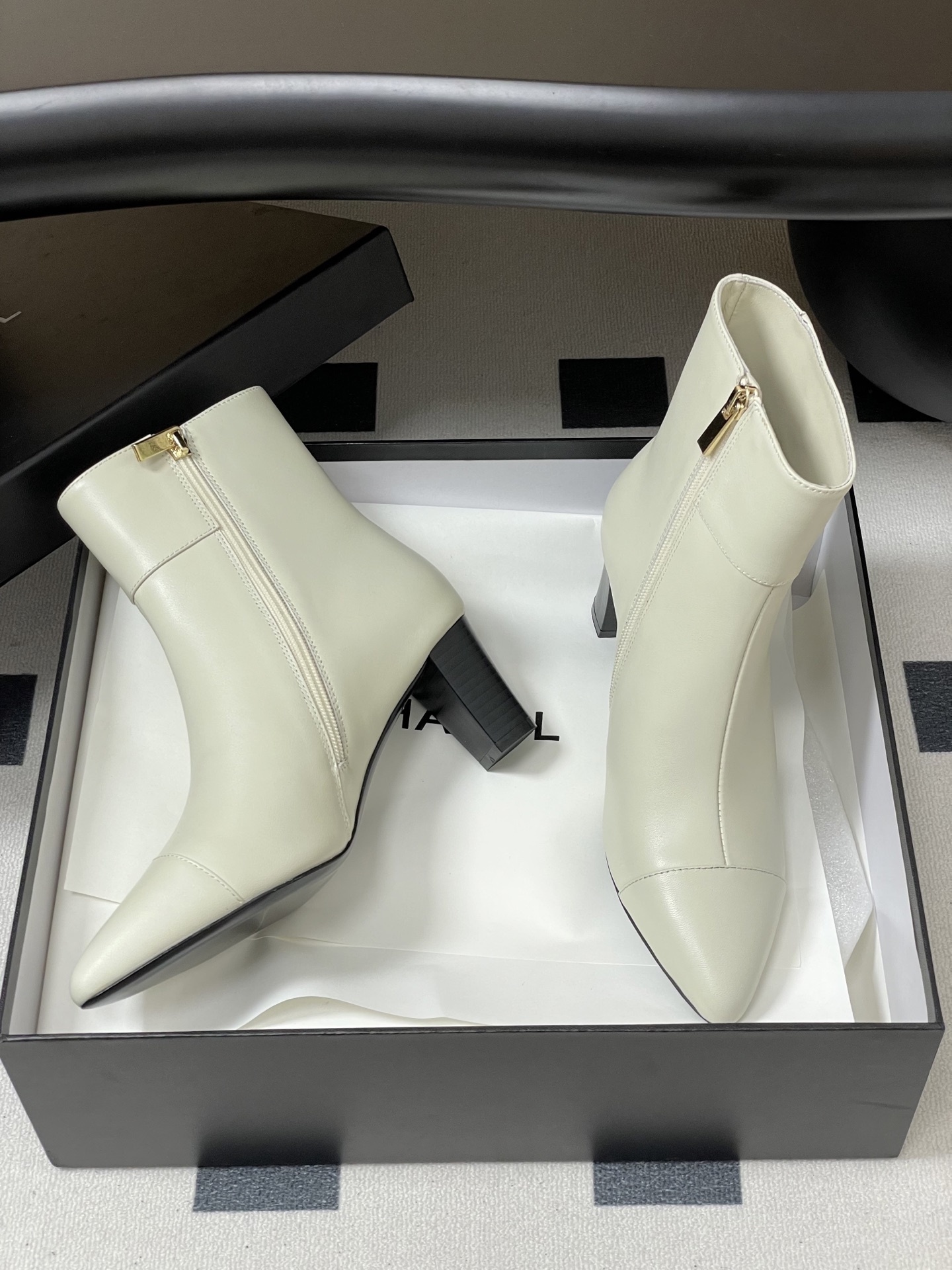Pair of creamy white leather ankle boots with gold lion head hardware and pointed toe on a black surface - Hình 6