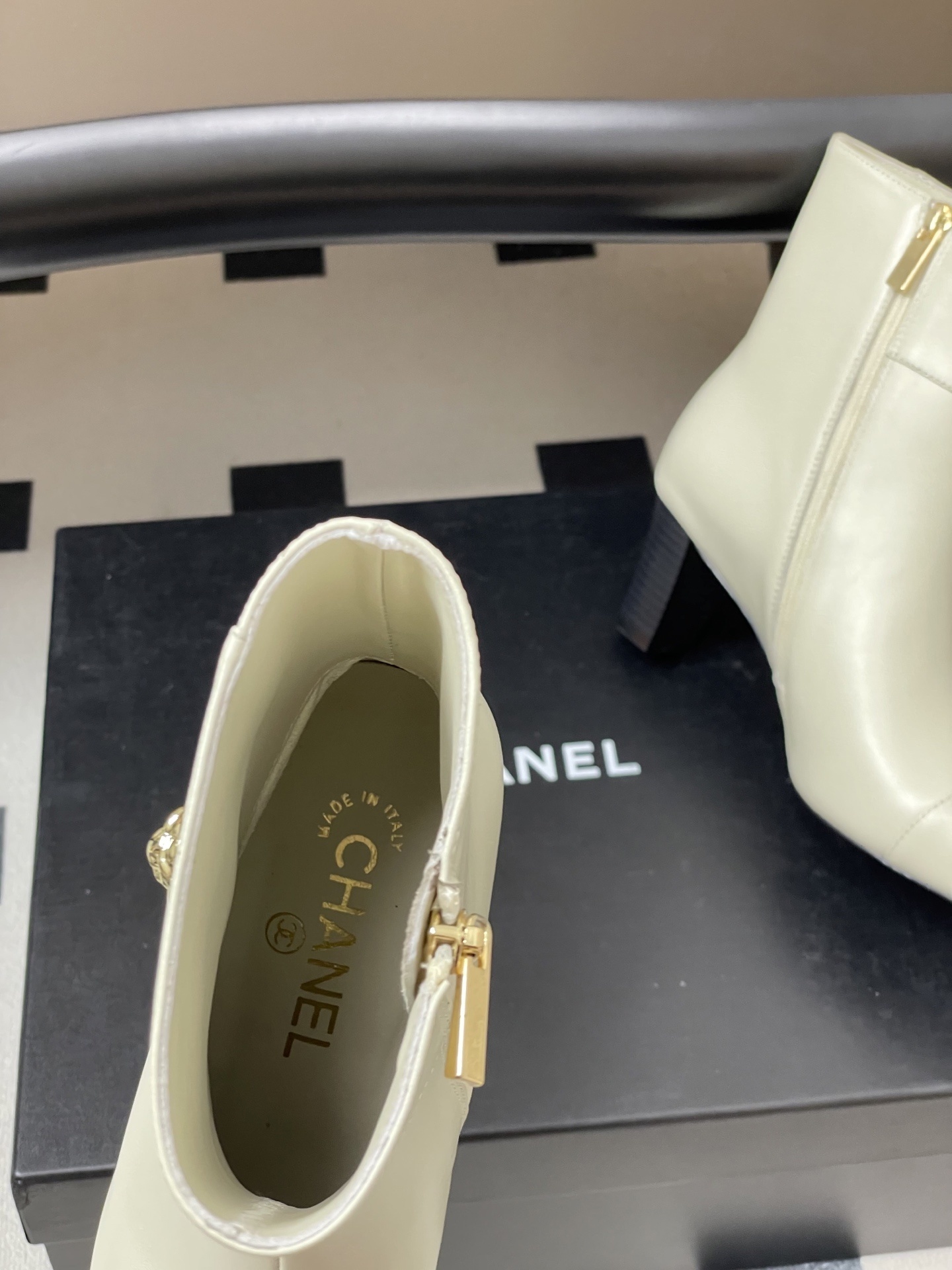 Pair of creamy white leather ankle boots with gold lion head hardware and pointed toe on a black surface - Hình 5