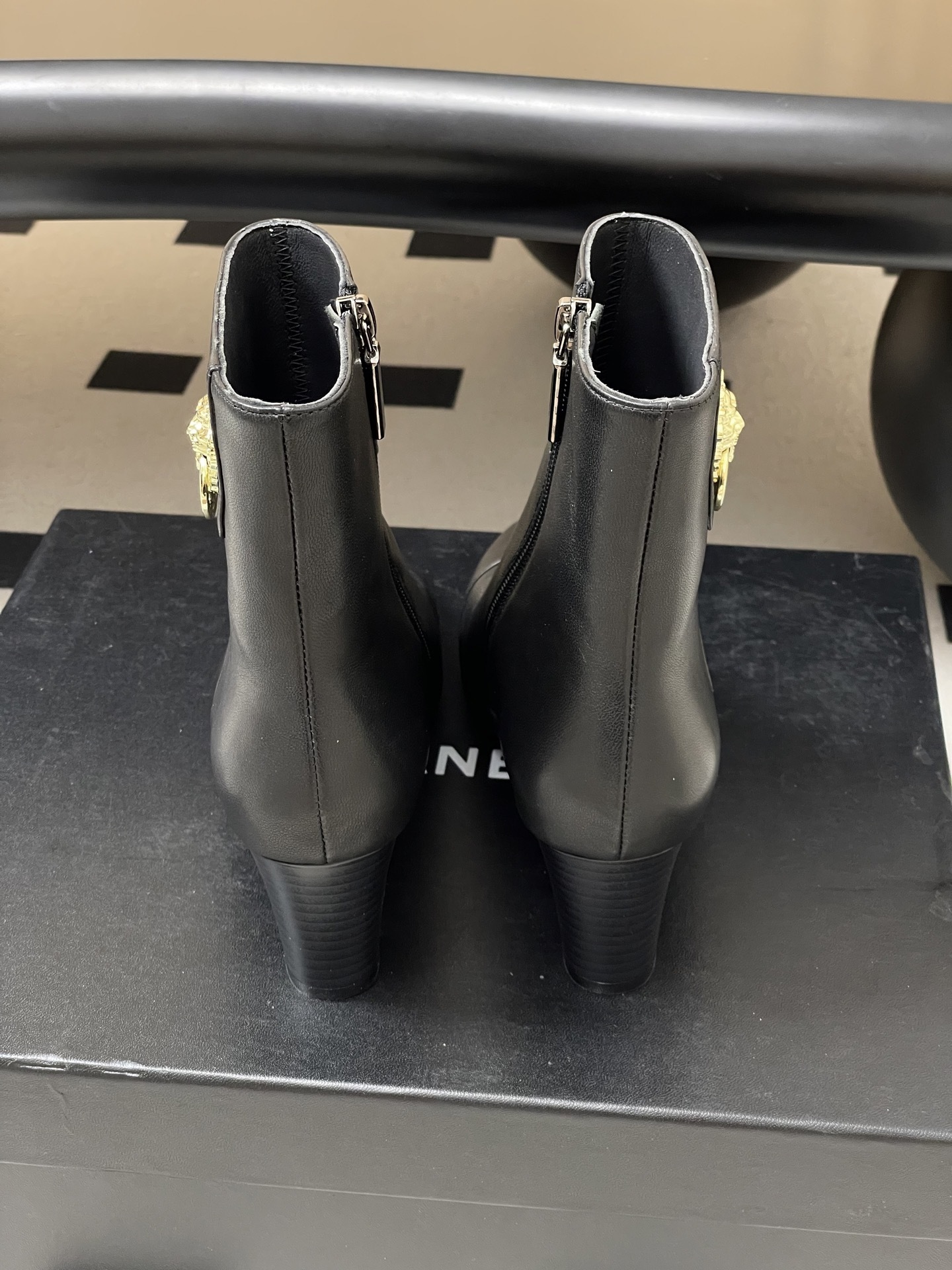 Pair of premium black leather ankle boots with pointed toes and gold lion head decorations on a black surface. - Hình 9