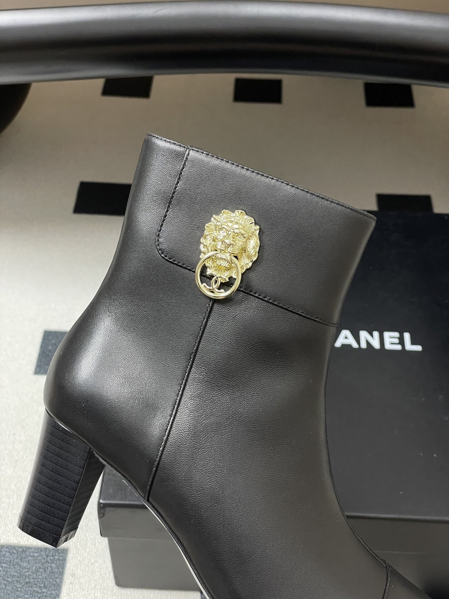Pair of premium black leather ankle boots with pointed toes and gold lion head decorations on a black surface. - Hình 7