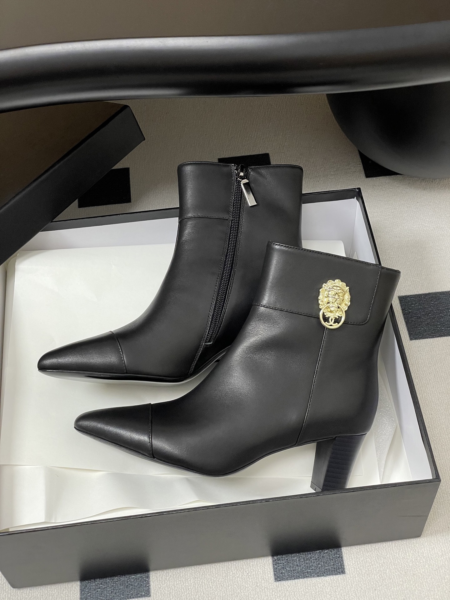 Pair of premium black leather ankle boots with pointed toes and gold lion head decorations on a black surface. - Hình 4