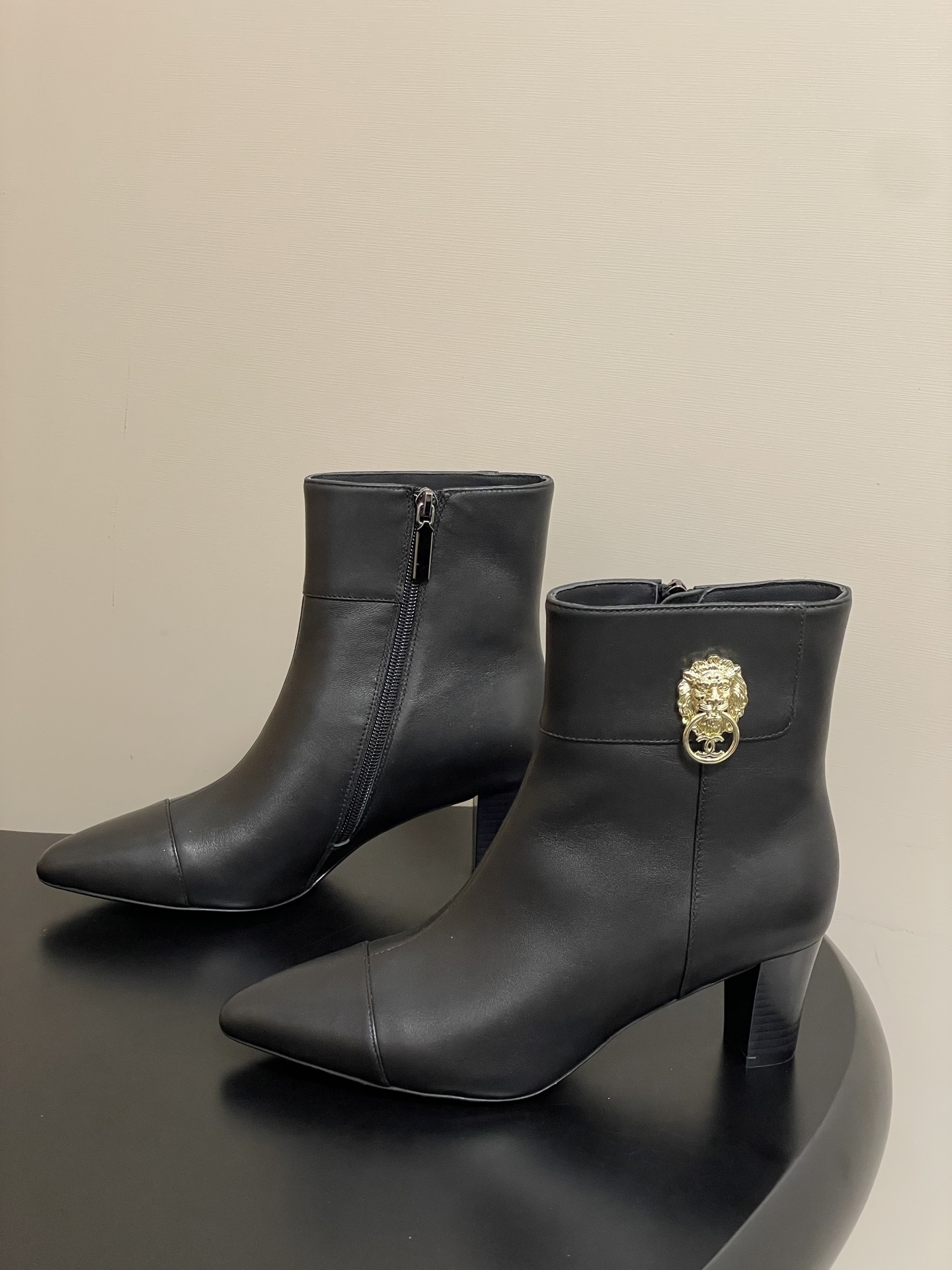 Pair of premium black leather ankle boots with pointed toes and gold lion head decorations on a black surface. - Hình 3