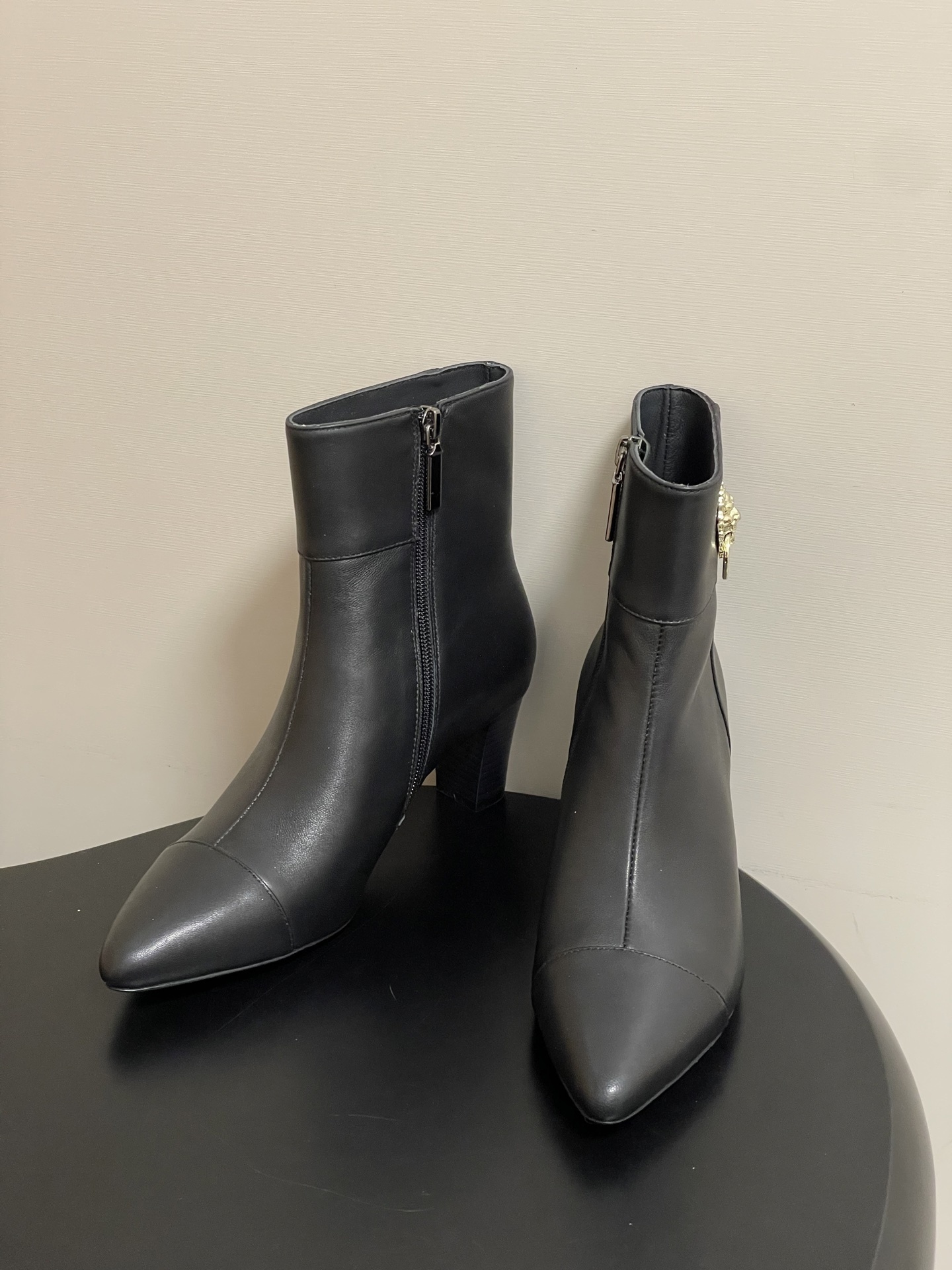 Pair of premium black leather ankle boots with pointed toes and gold lion head decorations on a black surface. - Hình 2
