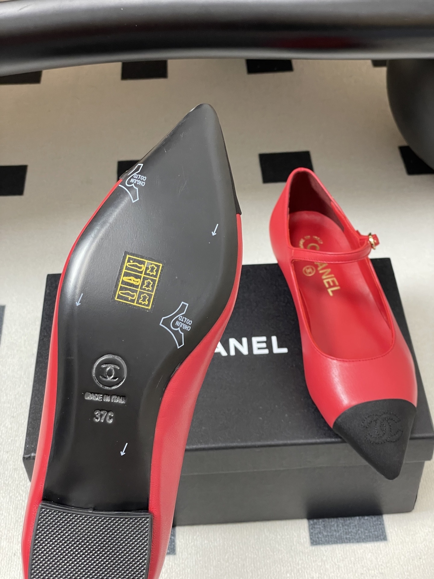 Pair of red Chanel Mary Jane leather flats with black pointed toe caps and gold CC logo on a black surface. - Hình 8