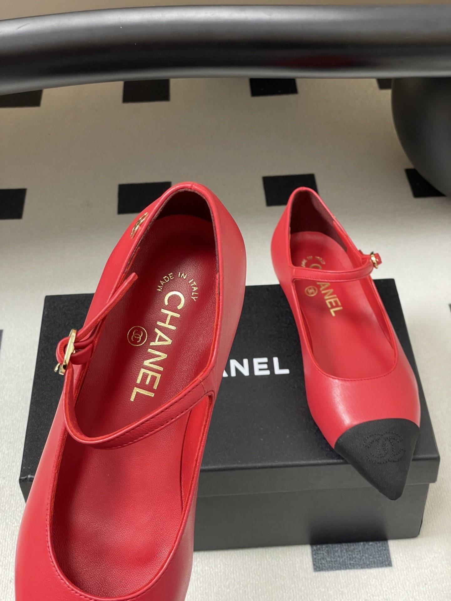Pair of red Chanel Mary Jane leather flats with black pointed toe caps and gold CC logo on a black surface. - Hình 7