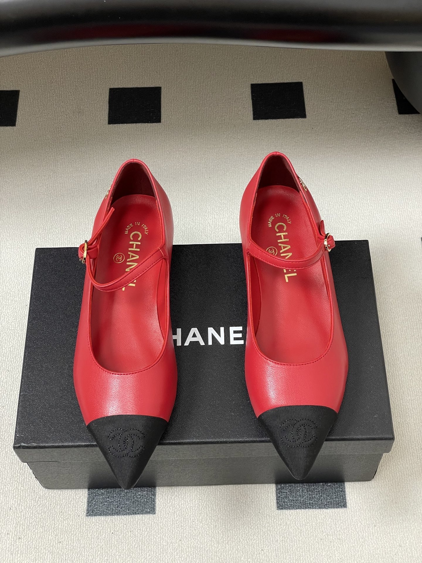 Pair of red Chanel Mary Jane leather flats with black pointed toe caps and gold CC logo on a black surface. - Hình 5