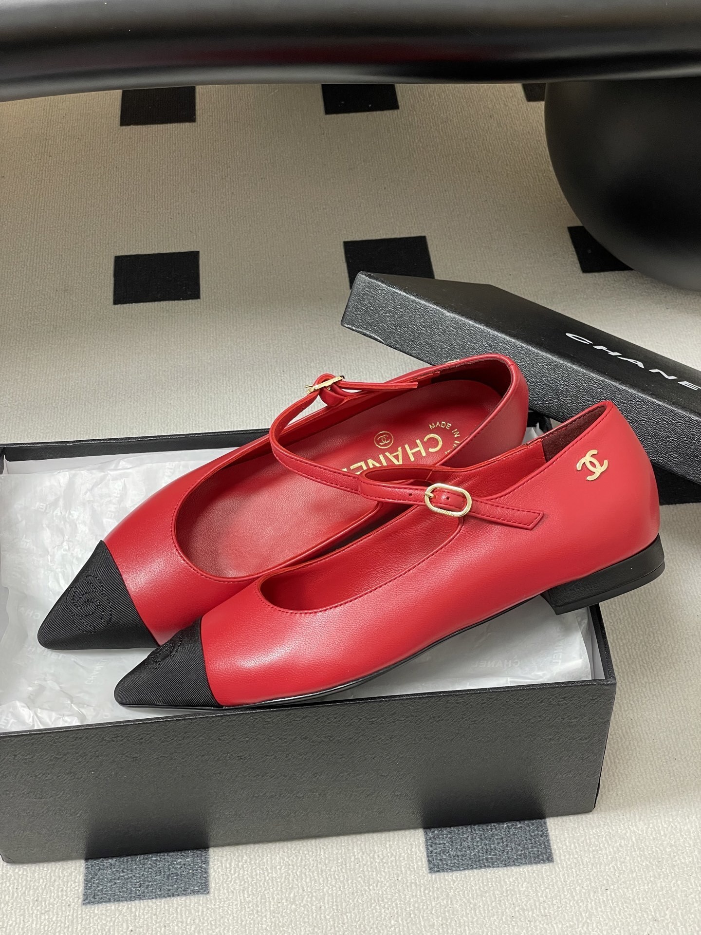 Pair of red Chanel Mary Jane leather flats with black pointed toe caps and gold CC logo on a black surface. - Hình 4