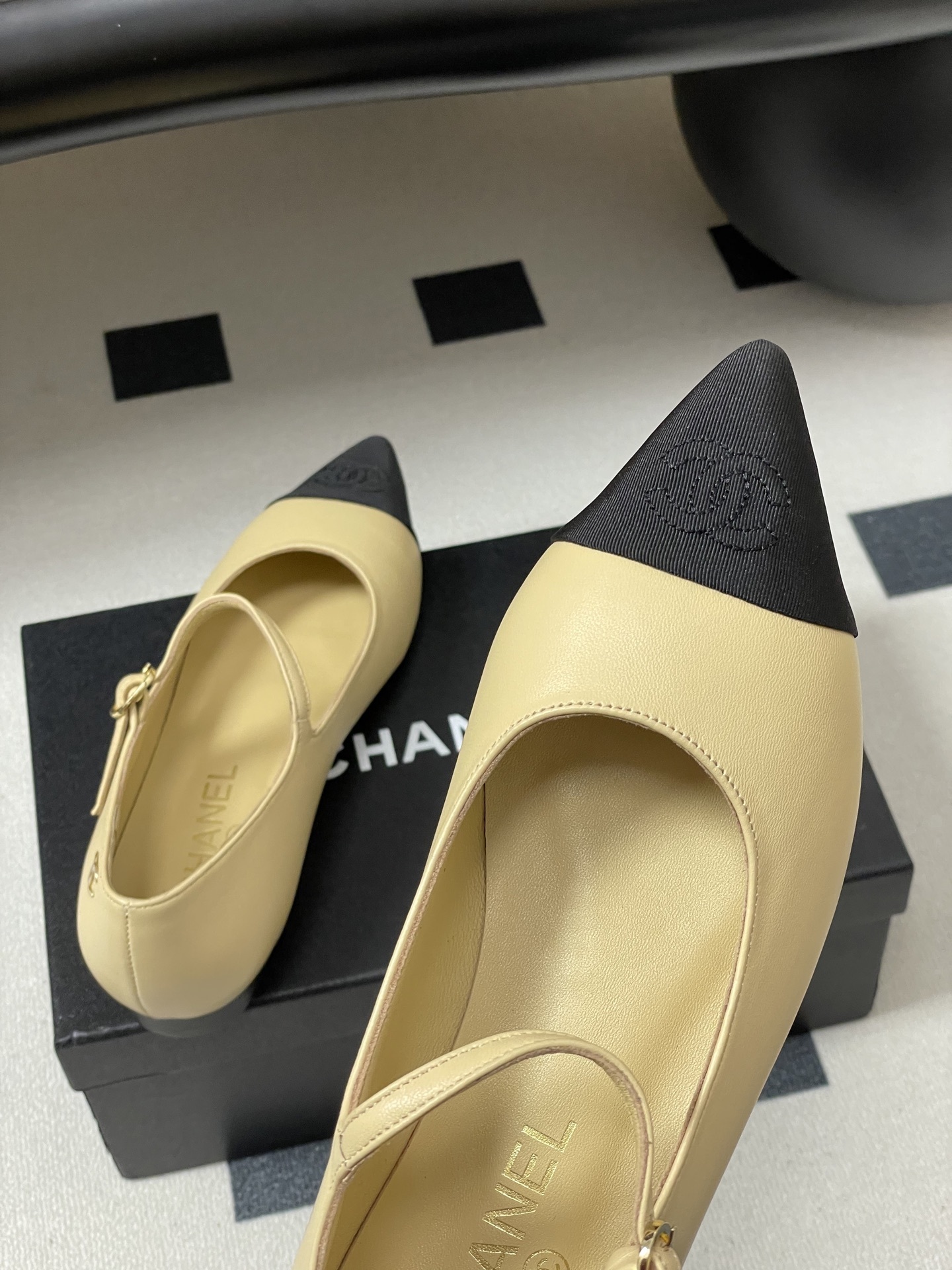 Chanel beige leather Mary Jane flats with black pointed cap toes and gold CC logo hardware on a black table. - Hình 9