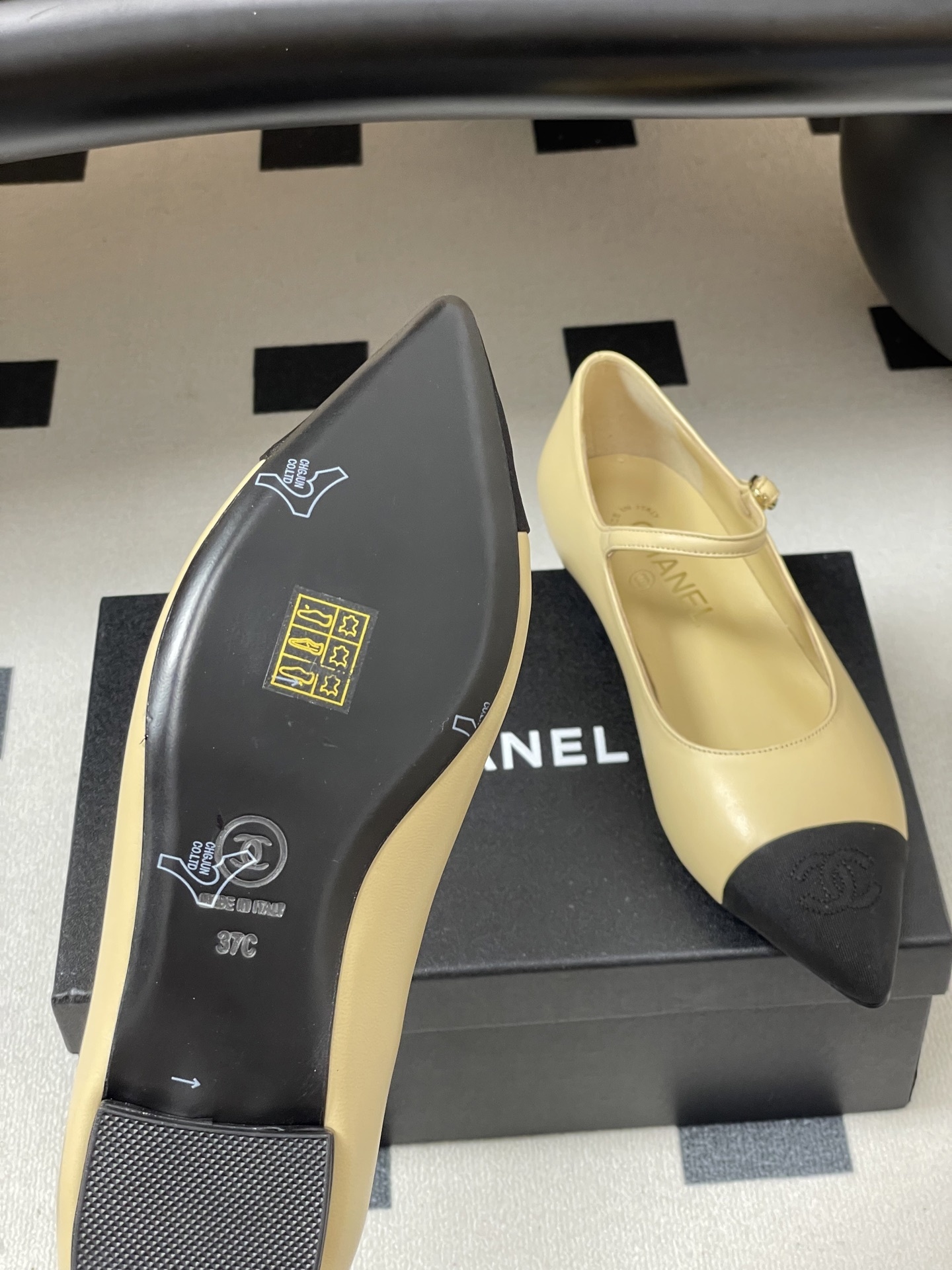 Chanel beige leather Mary Jane flats with black pointed cap toes and gold CC logo hardware on a black table. - Hình 8
