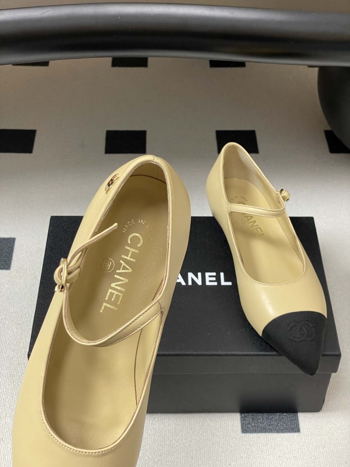 Chanel beige leather Mary Jane flats with black pointed cap toes and gold CC logo hardware on a black table. - Hình 7