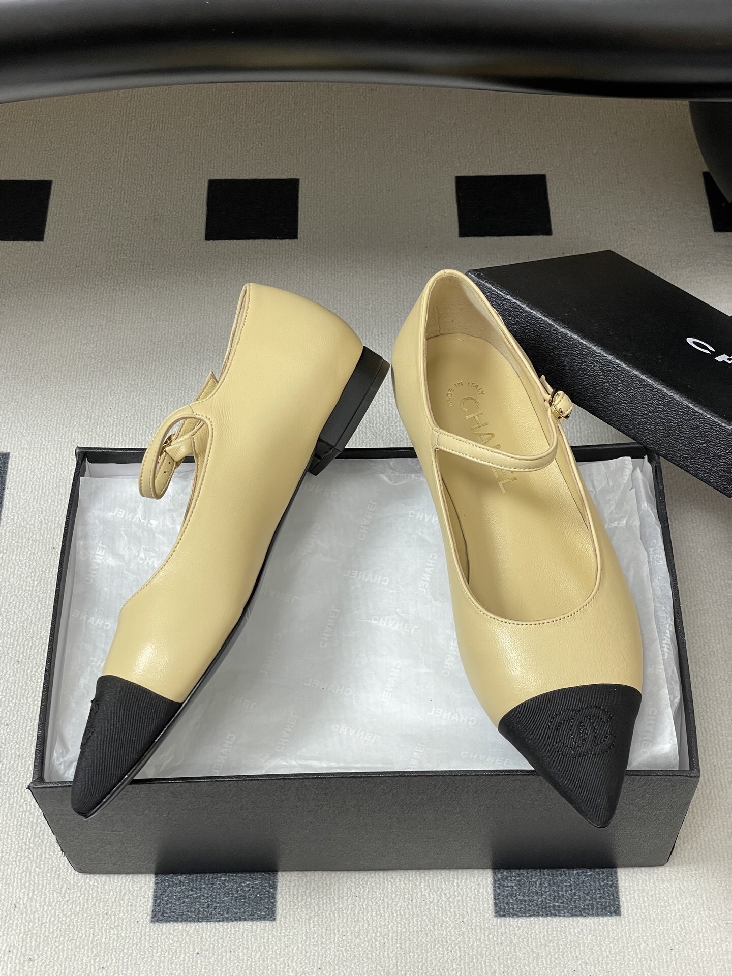 Chanel beige leather Mary Jane flats with black pointed cap toes and gold CC logo hardware on a black table. - Hình 6