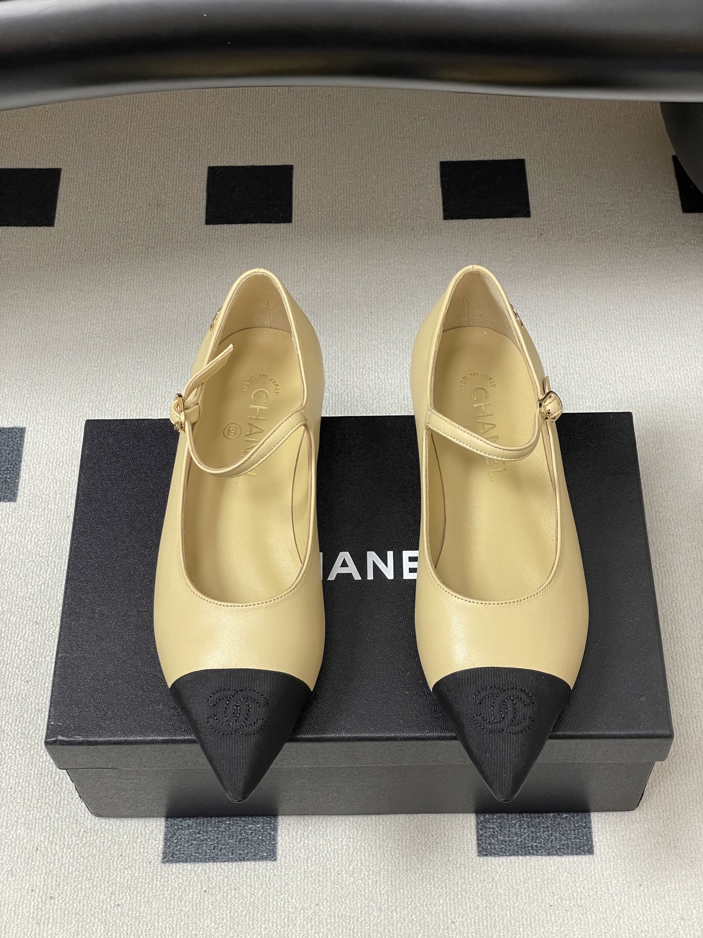 Chanel beige leather Mary Jane flats with black pointed cap toes and gold CC logo hardware on a black table. - Hình 5
