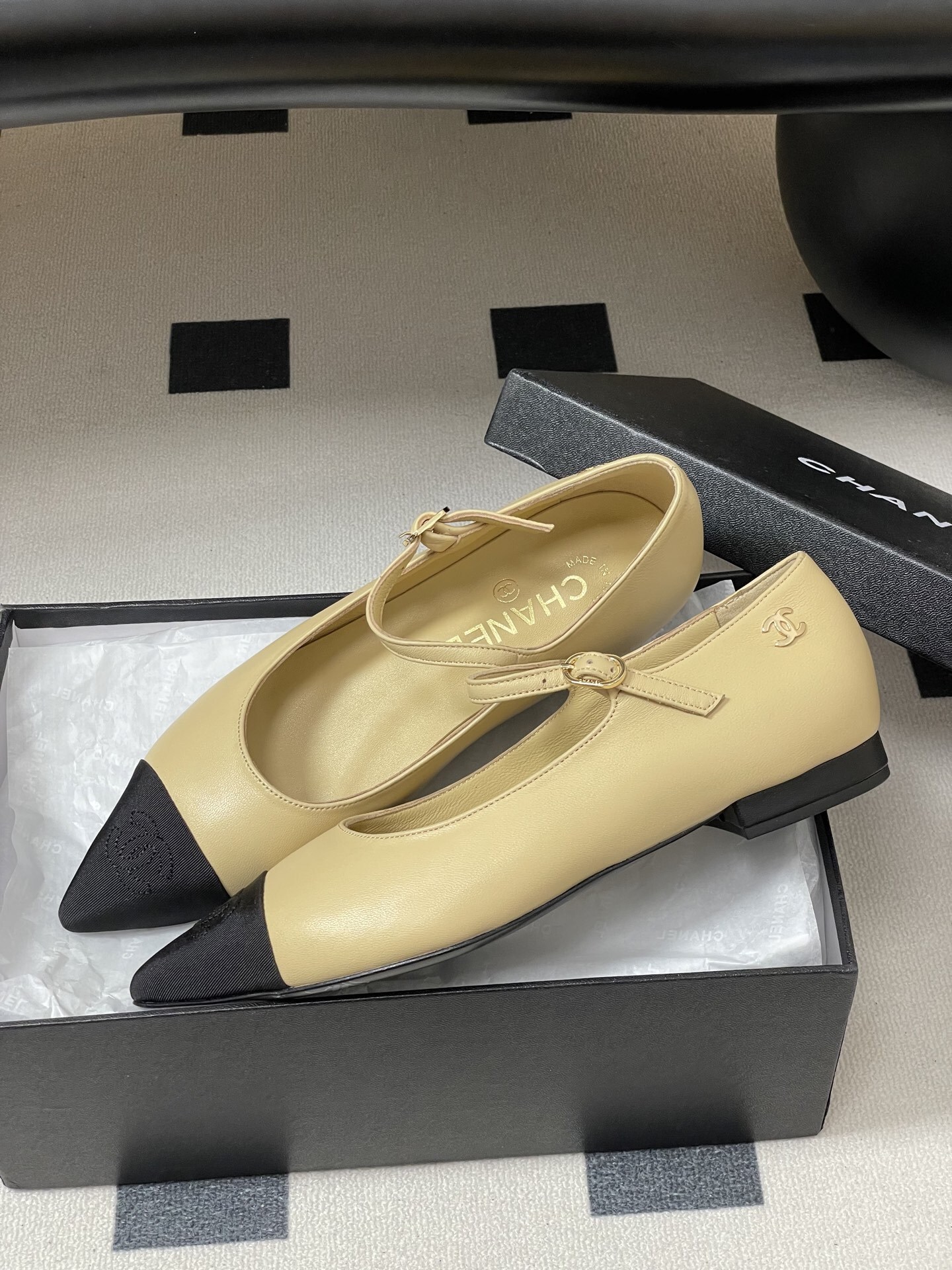 Chanel beige leather Mary Jane flats with black pointed cap toes and gold CC logo hardware on a black table. - Hình 4