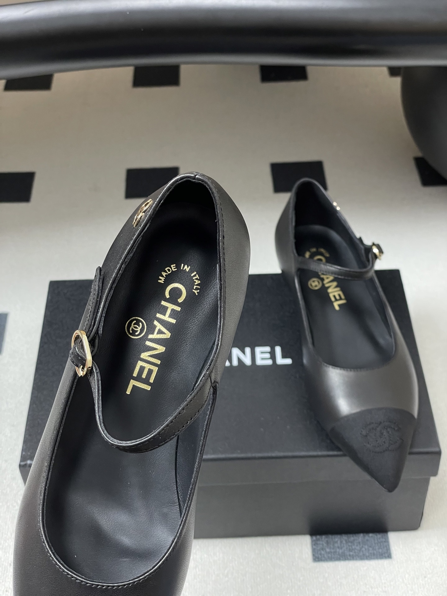Pair of Chanel black leather Mary Jane pointed toe flats with gold CC logo and buckled strap on a black surface - Hình 7