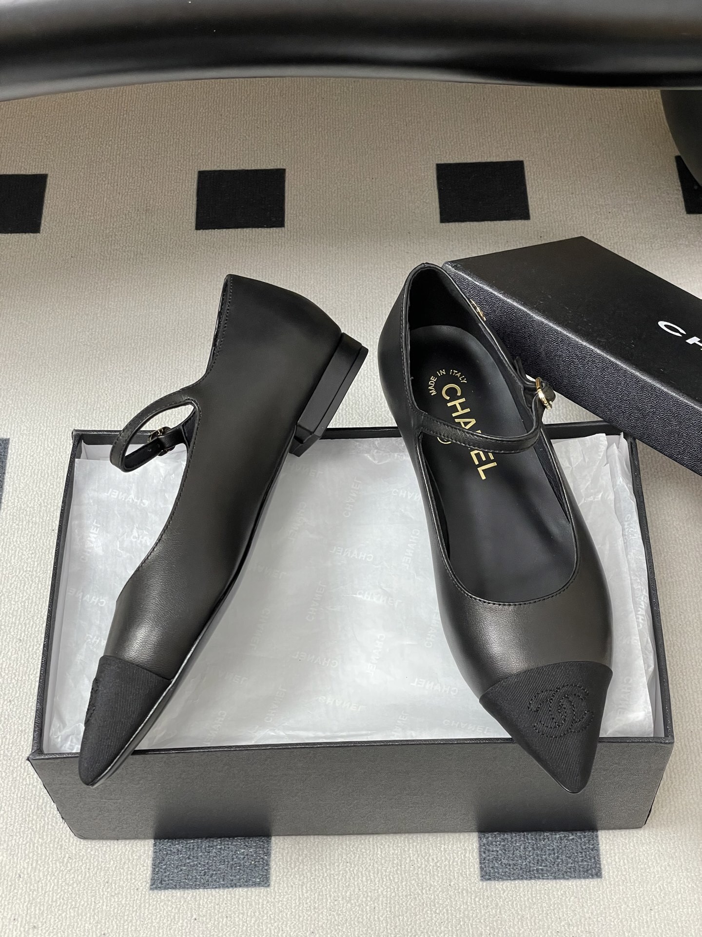 Pair of Chanel black leather Mary Jane pointed toe flats with gold CC logo and buckled strap on a black surface - Hình 6