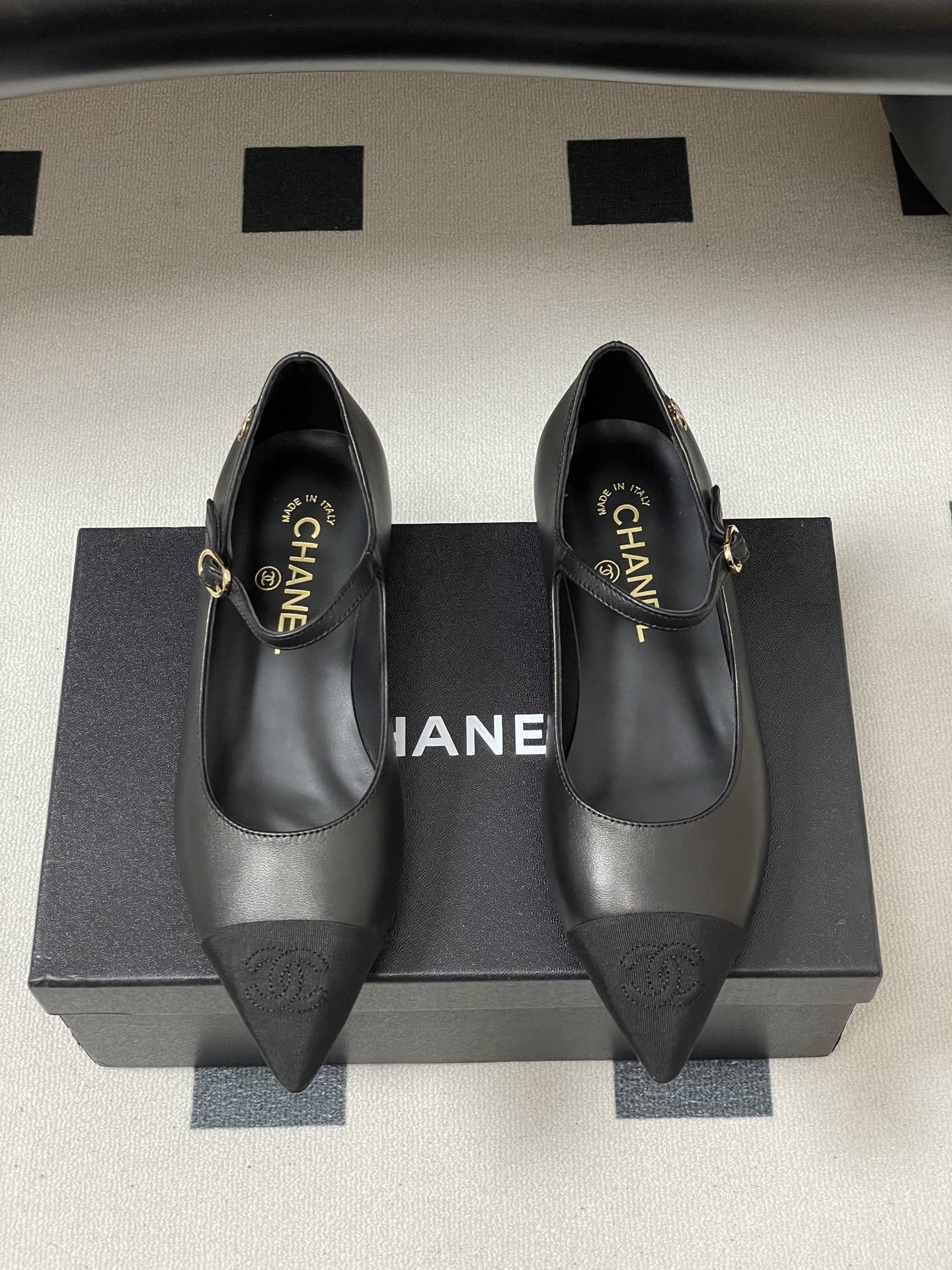 Pair of Chanel black leather Mary Jane pointed toe flats with gold CC logo and buckled strap on a black surface - Hình 5
