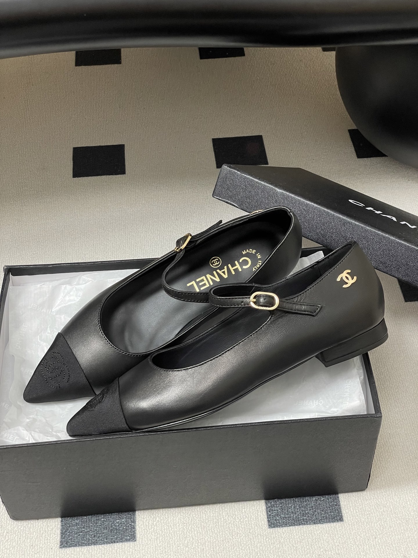 Pair of Chanel black leather Mary Jane pointed toe flats with gold CC logo and buckled strap on a black surface - Hình 4