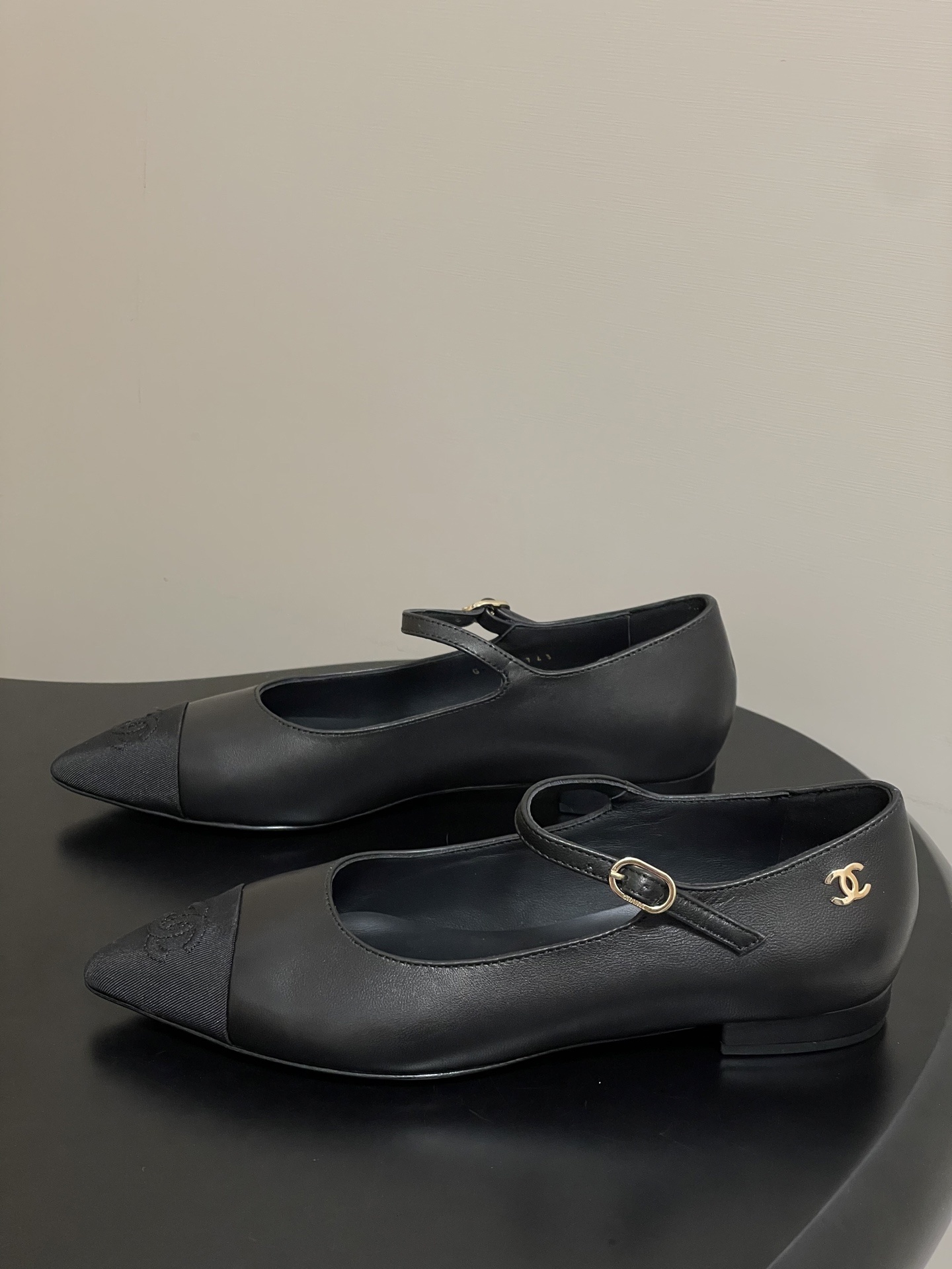 Pair of Chanel black leather Mary Jane pointed toe flats with gold CC logo and buckled strap on a black surface - Hình 3