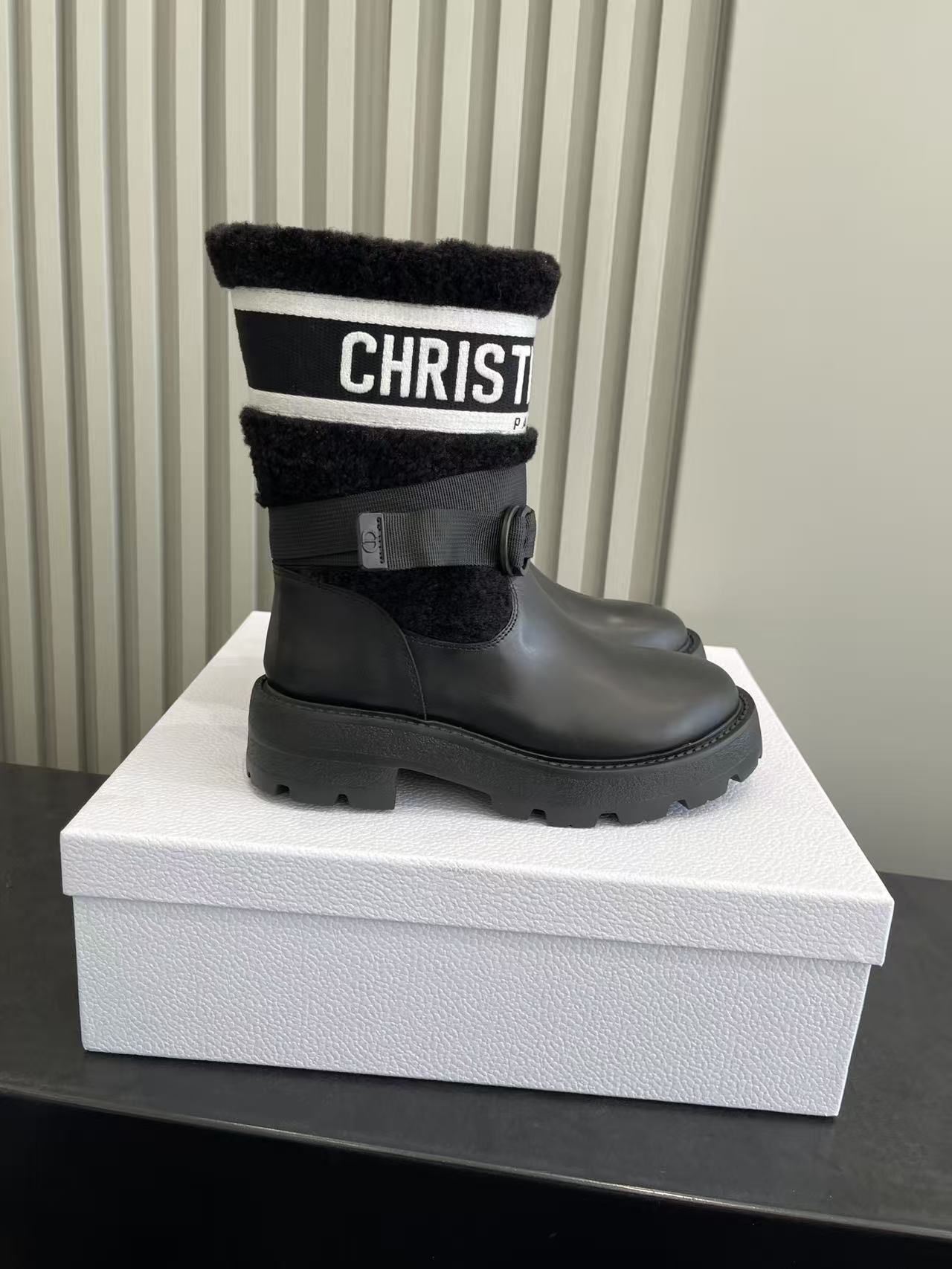 A pair of Dior D-Major black calfskin and shearling ankle boots with white Christian Dior Paris signature logo on a white box.