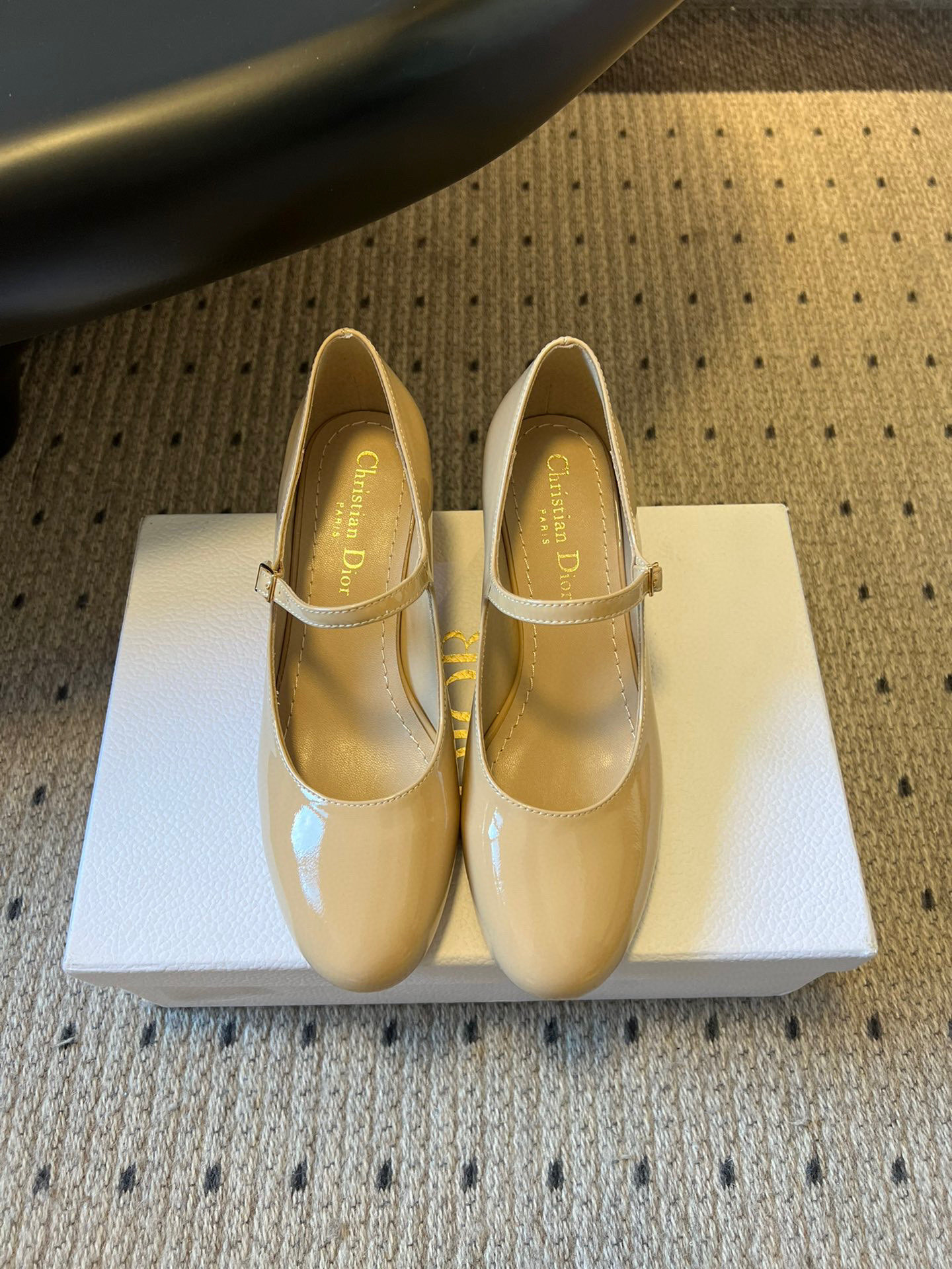 A pair of Christian Dior nude patent leather Mary Jane pumps with block heels resting on a white Dior shoebox.