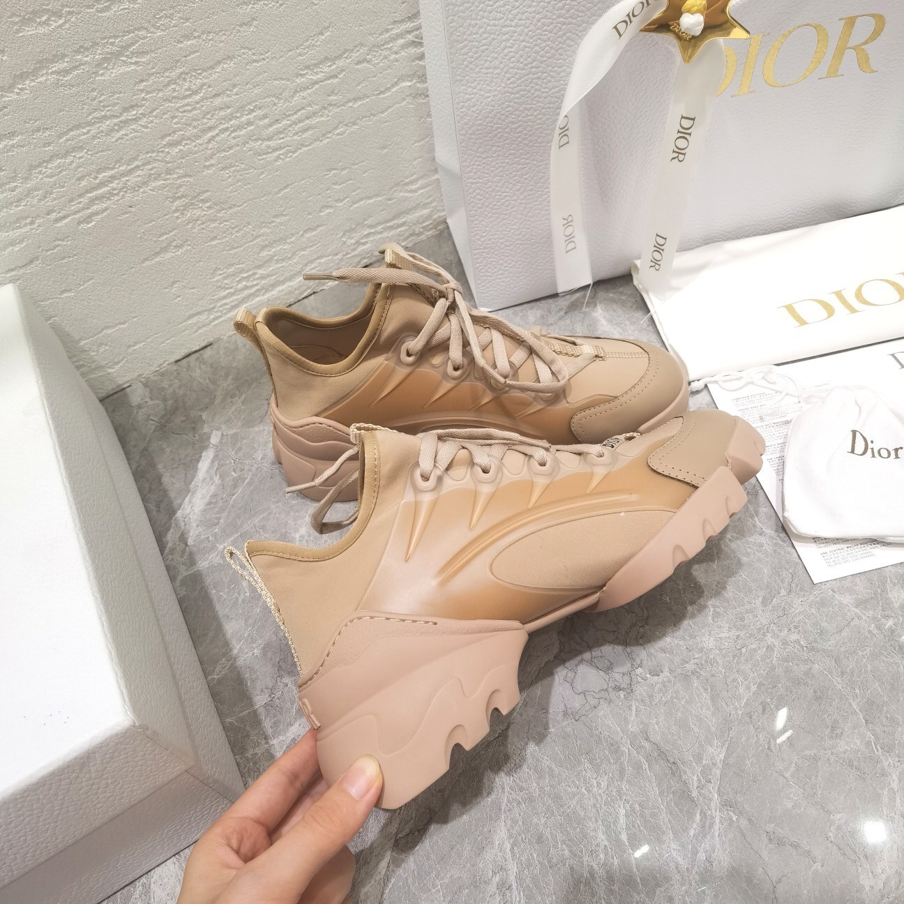 A pair of Dior D-Connect sneakers in nude technical fabric shown with original Dior shopping bag and white luxury packaging.