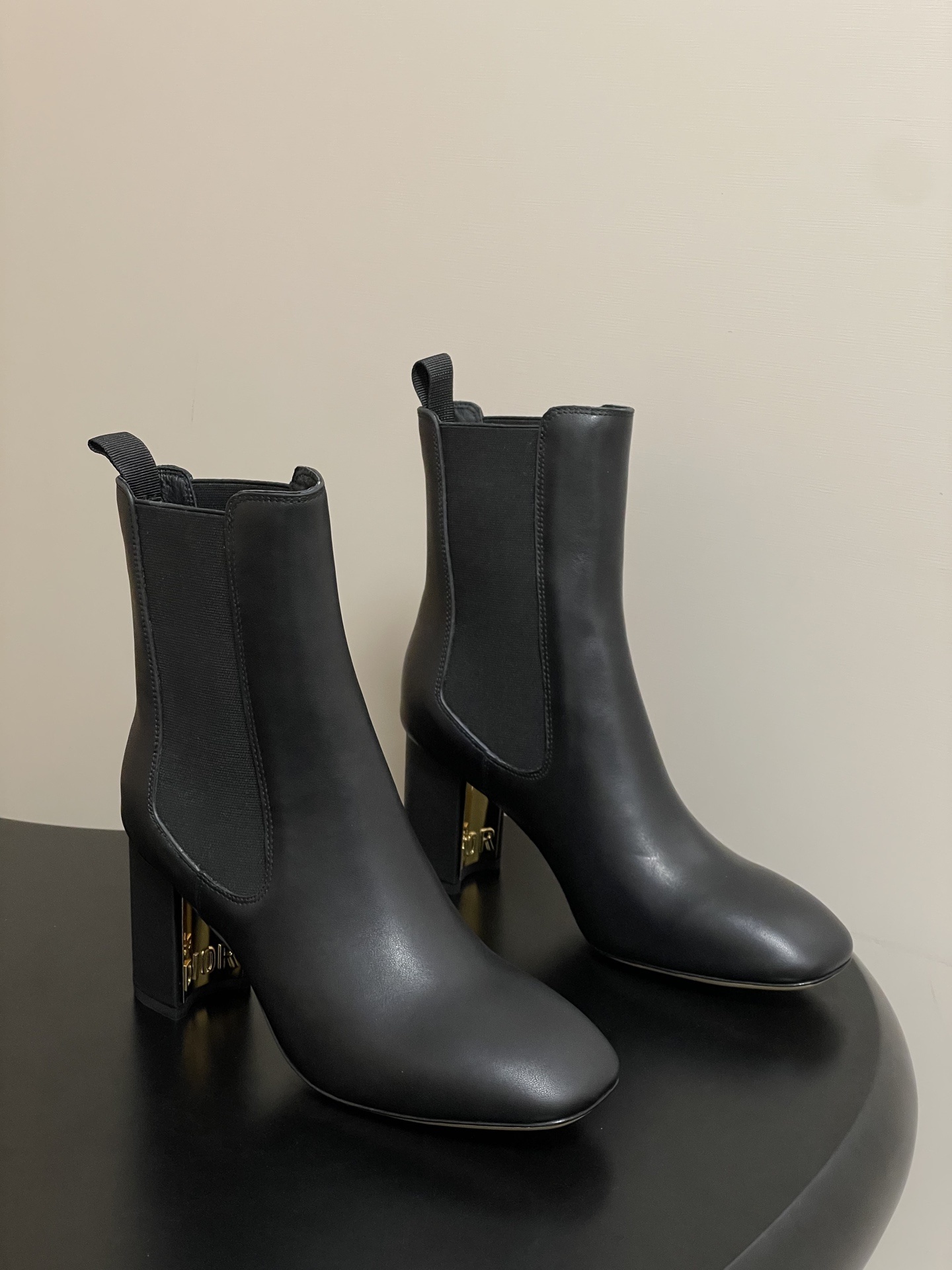 A pair of Dior black leather ankle boots with elastic side panels and a gold-finish DIOR logo inside the block heel.