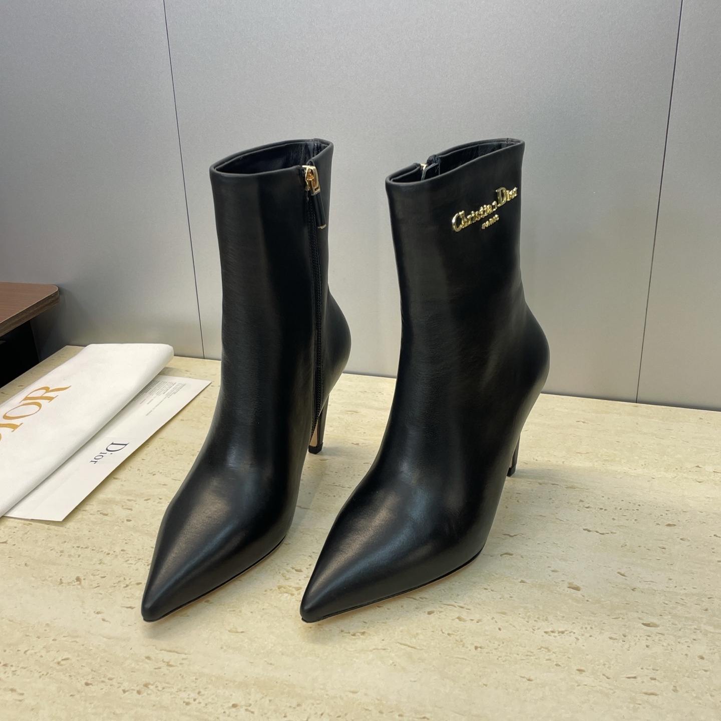 A pair of Christian Dior black leather ankle boots featuring a pointed toe, stiletto heel, and gold-tone Christian Dior Paris logo.