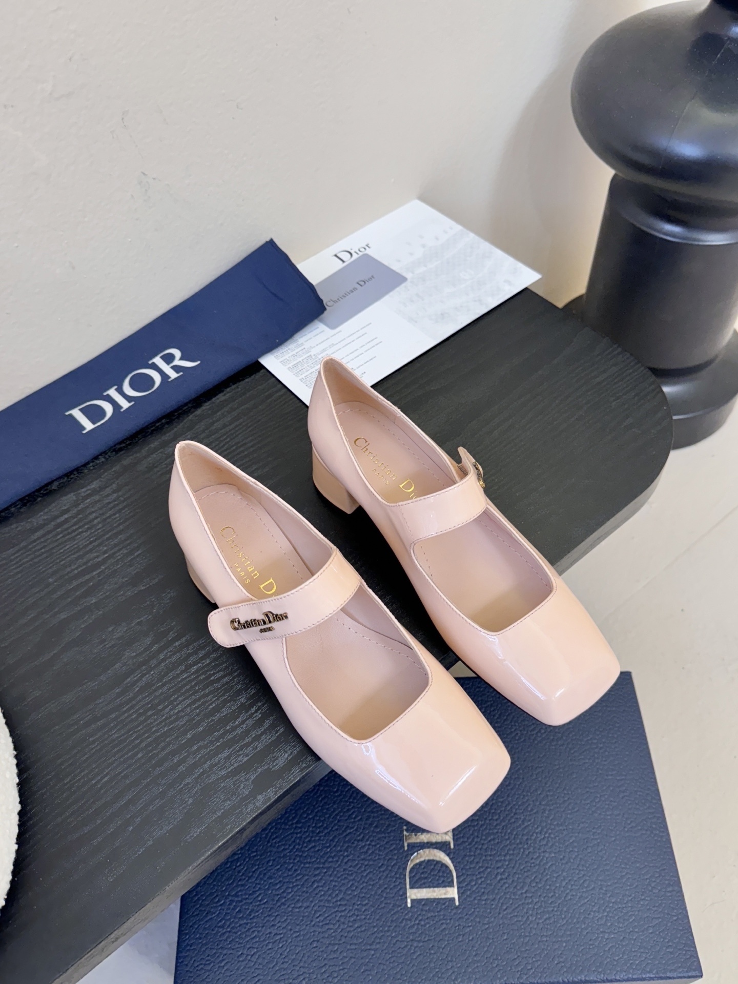 A pair of Christian Dior nude patent leather Mary Jane pumps with block heels and gold-tone signature straps displayed on a dark surface