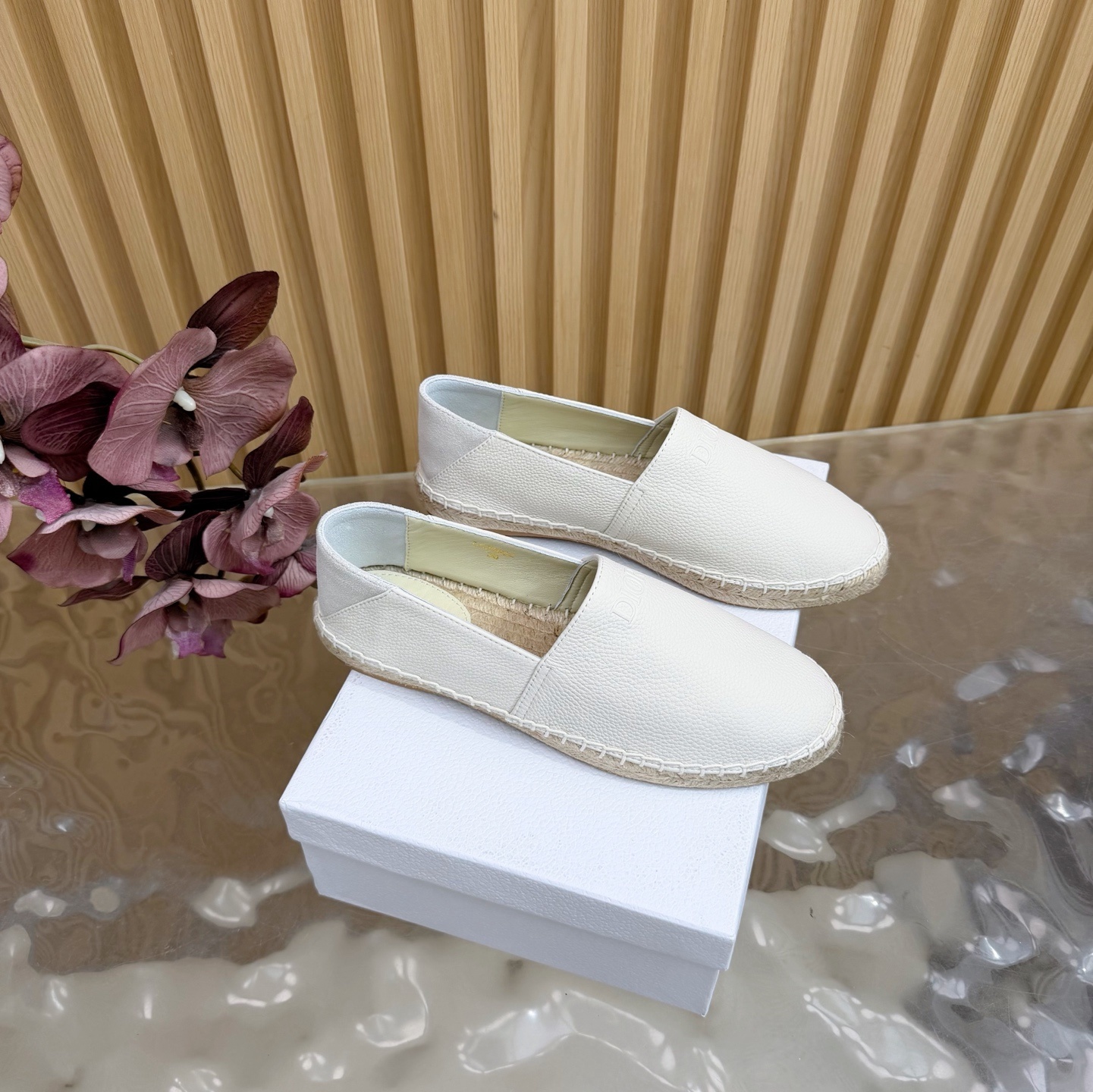 Pair of white Dior Granville espadrilles in grained calfskin with embossed logo sitting on a white Dior shoebox.