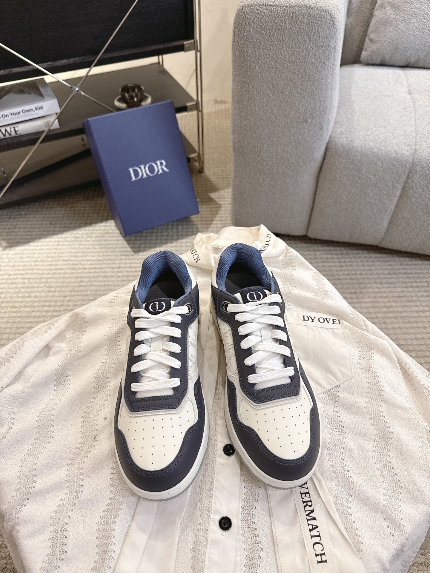 Dior B27 low-top sneakers in navy blue and white leather with Oblique canvas detailing displayed on a white lace garment