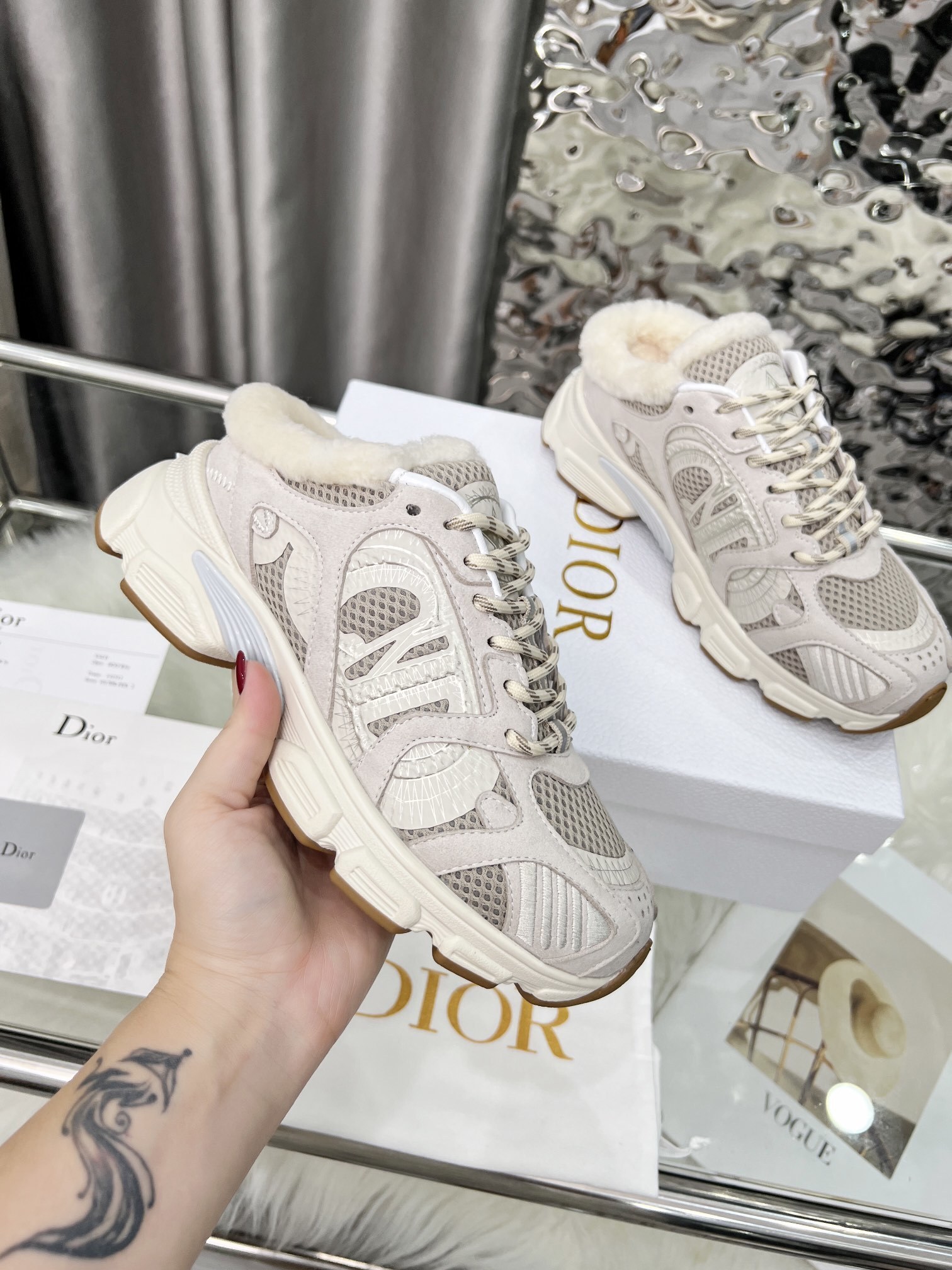 A pair of Dior Vibe beige sneakers with white shearling lining and chunky soles placed on a white Dior brand box.